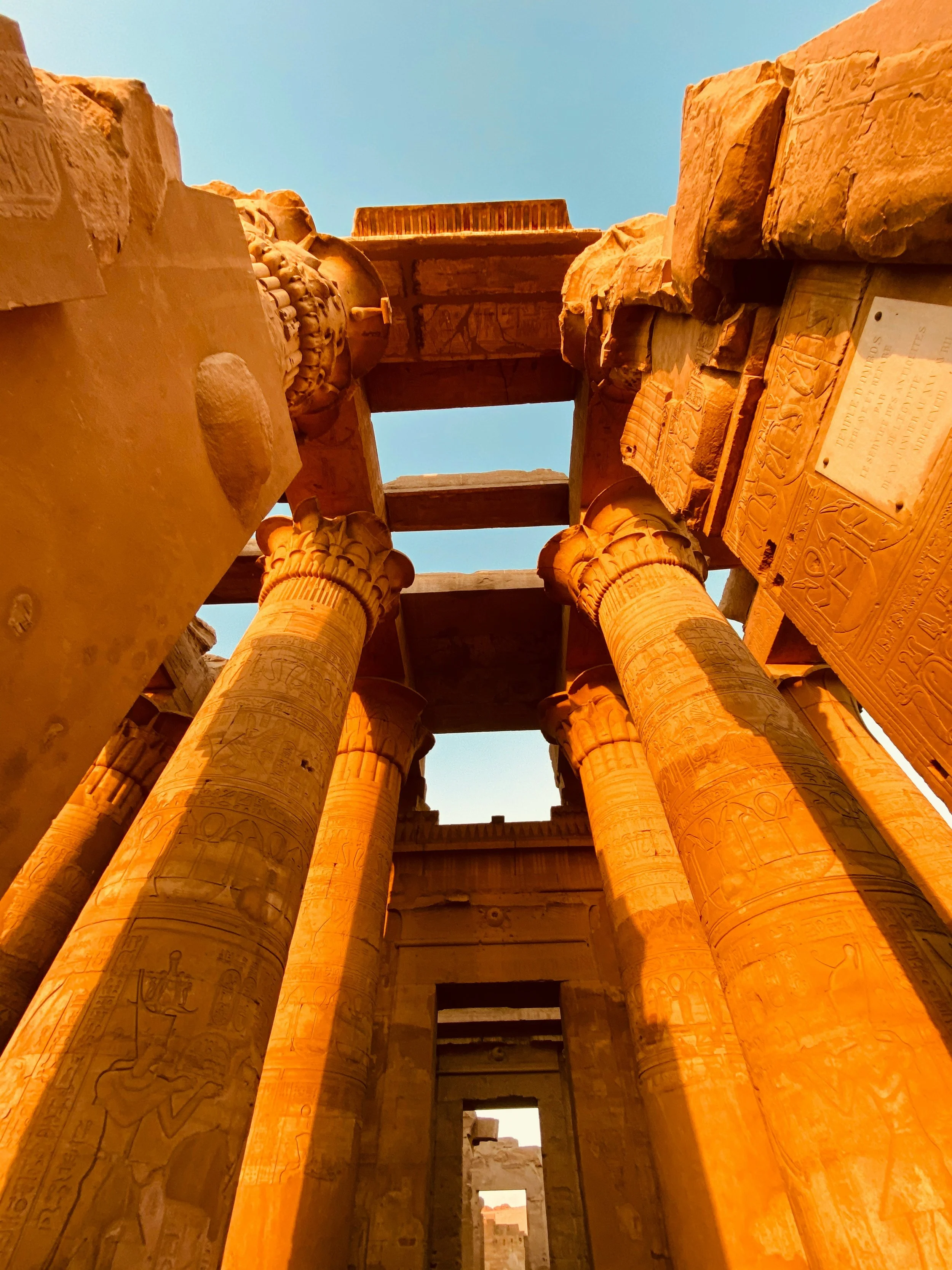 Looking upward at ancient Egyptian stone columns and hieroglyphics in a temple with a clear blue sky above.