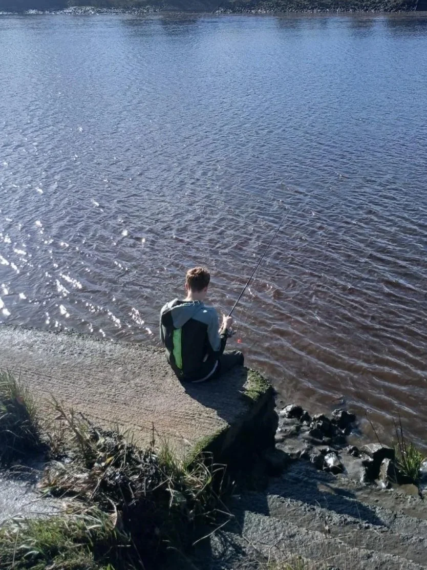 A pupil sitting on the riverbank, fishing on the Tyne in the sunshine