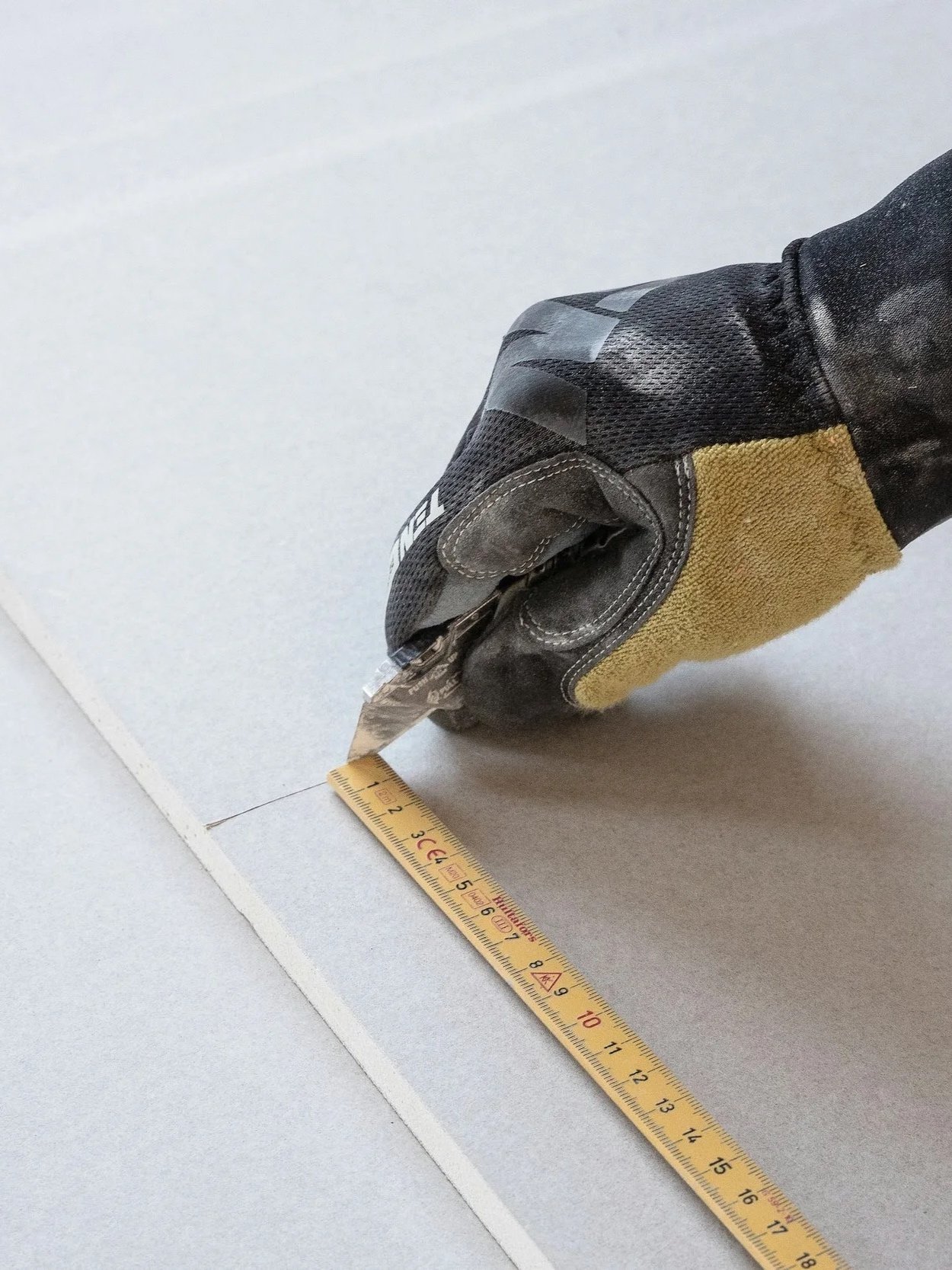A gloved hand holding a measuring tape on a flat surface with a ruler, used for size measurement.