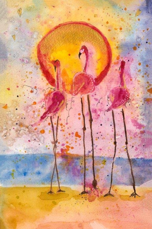 Watercolor painting of three pink flamingos standing on a beach in front of a setting sun, against a colorful sky with splashes of pink, orange, yellow, and blue.