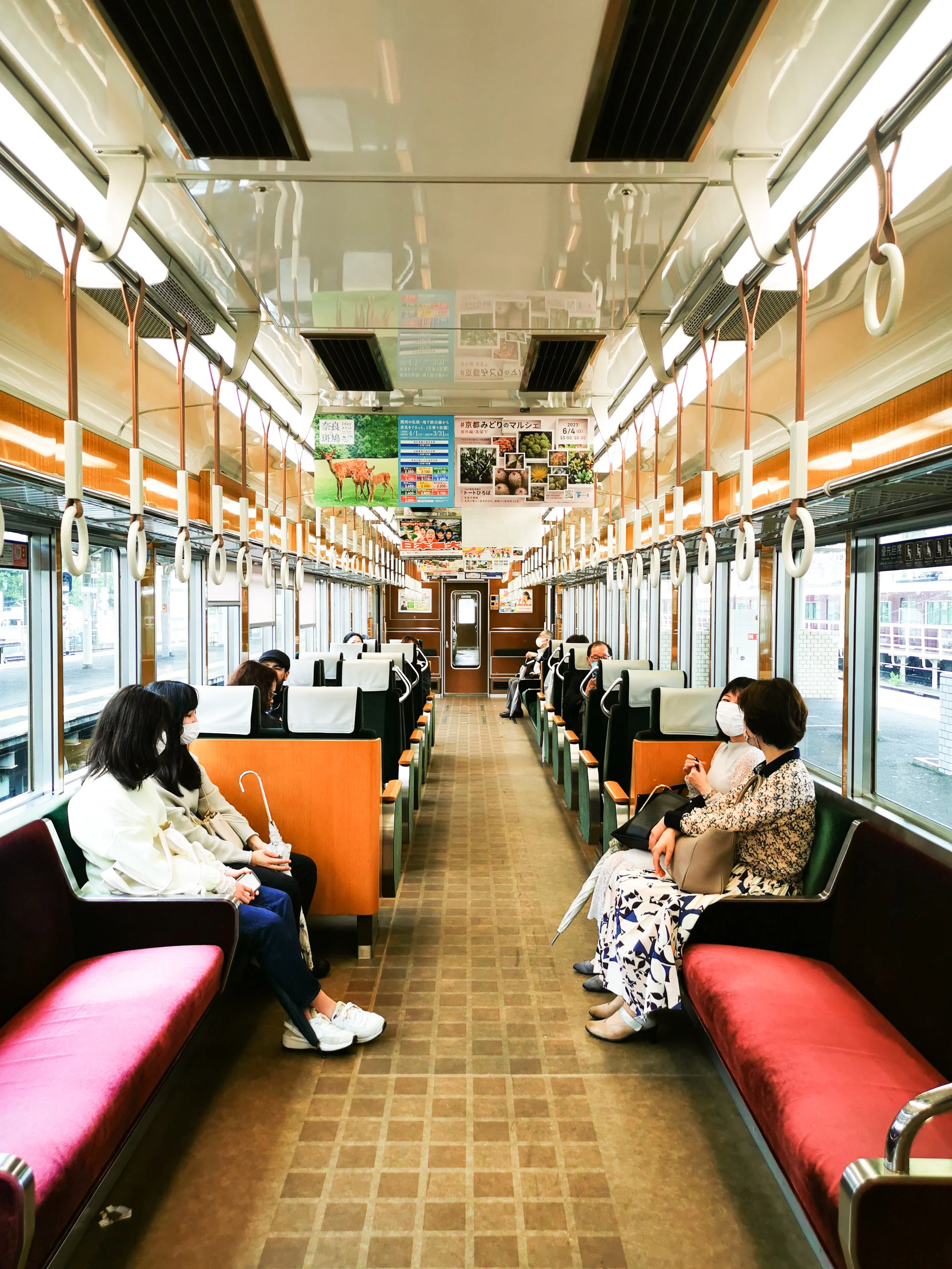 Intérieur d'un train avec des passagers assis, portant des masques, fenêtres grandes avec vue extérieure, affiches publicitaires suspendues au plafond