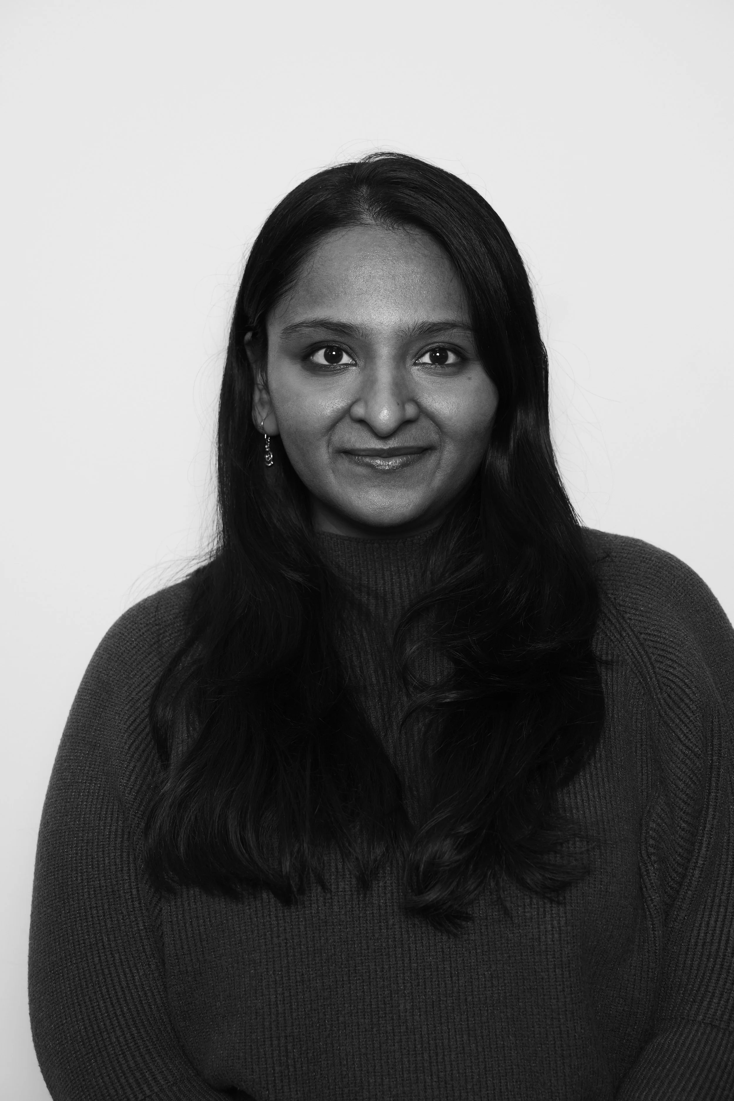 Black and white portrait of a woman with long dark hair, wearing a sweater, smiling gently, against a plain white background.