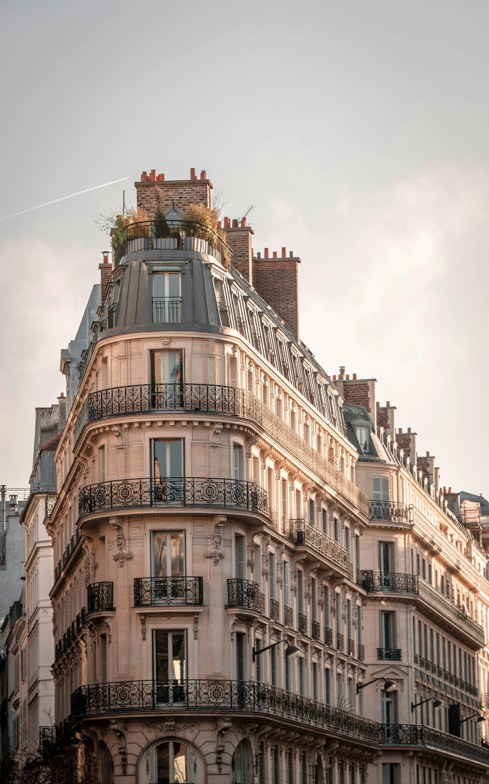 Immeuble parisien avec balcons en fer forgé et façades en pierre, vue de l'angle avec plusieurs étages et toits en zinc, le ciel en arrière-plan.