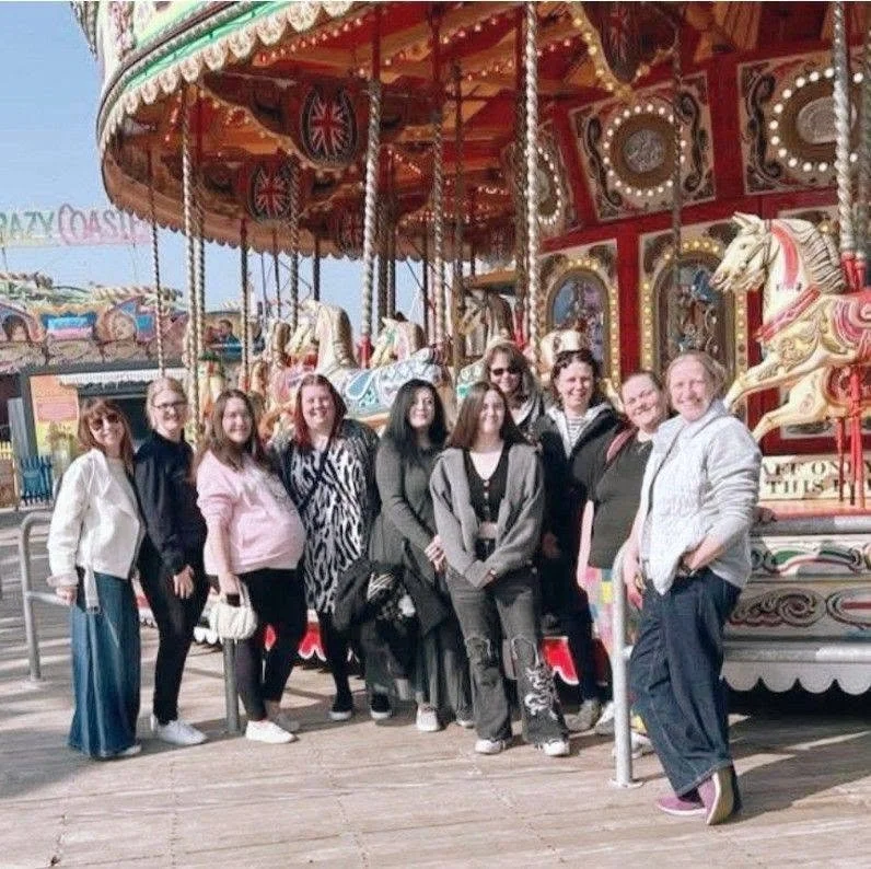 A group of women standing in front of a vintage carousel ride at an amusement park.