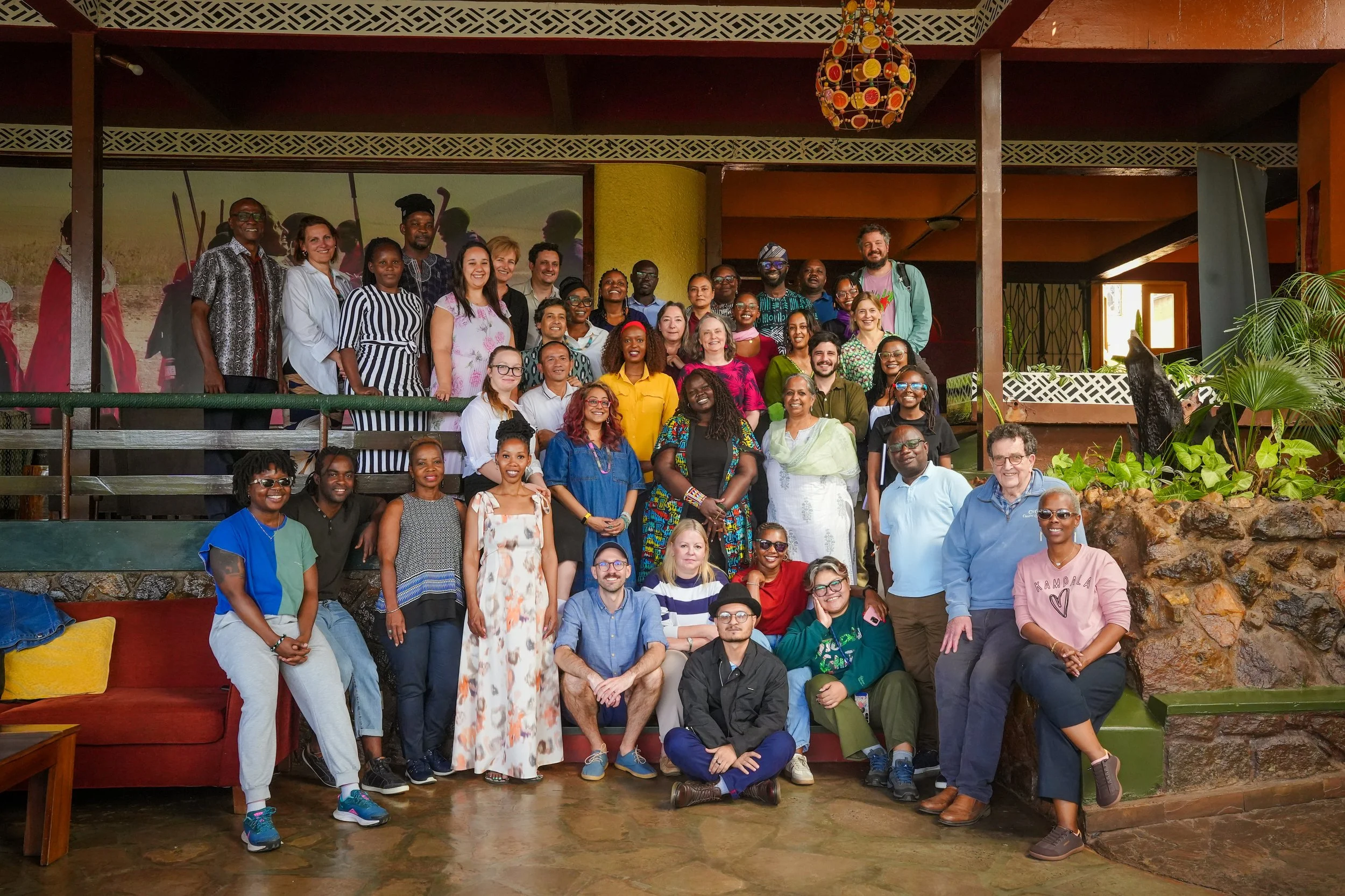 Group photo of diverse people standing and sitting on steps indoors, smiling.