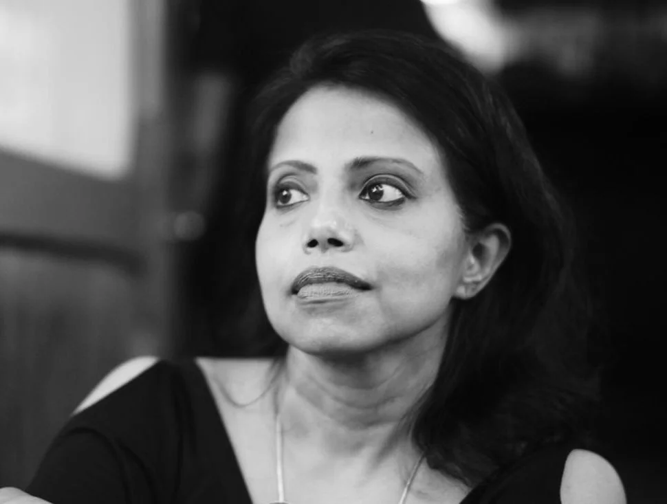 A black and white photo of a woman with dark hair looking to the side with a neutral expression.