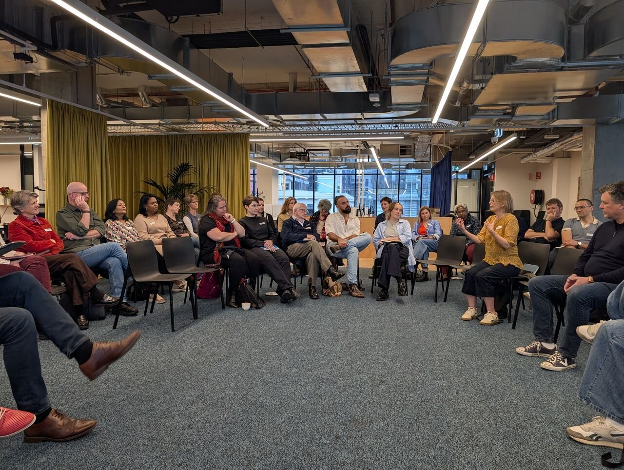 A diverse group of people seated in a circle in a modern conference room, engaged in a discussion.