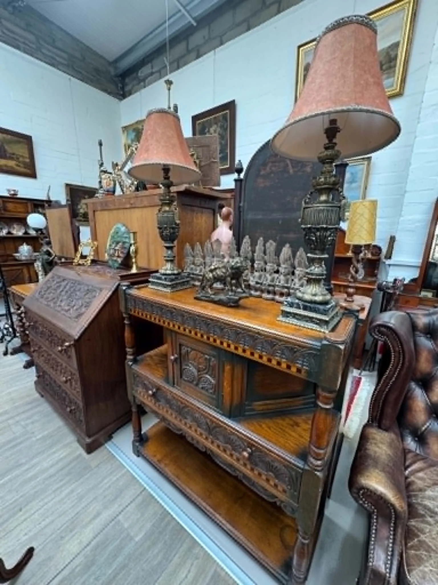 Various vintage and antique furniture and decor items displayed in an antique shop, including lamps, a chessboard, paintings, and wooden furniture.