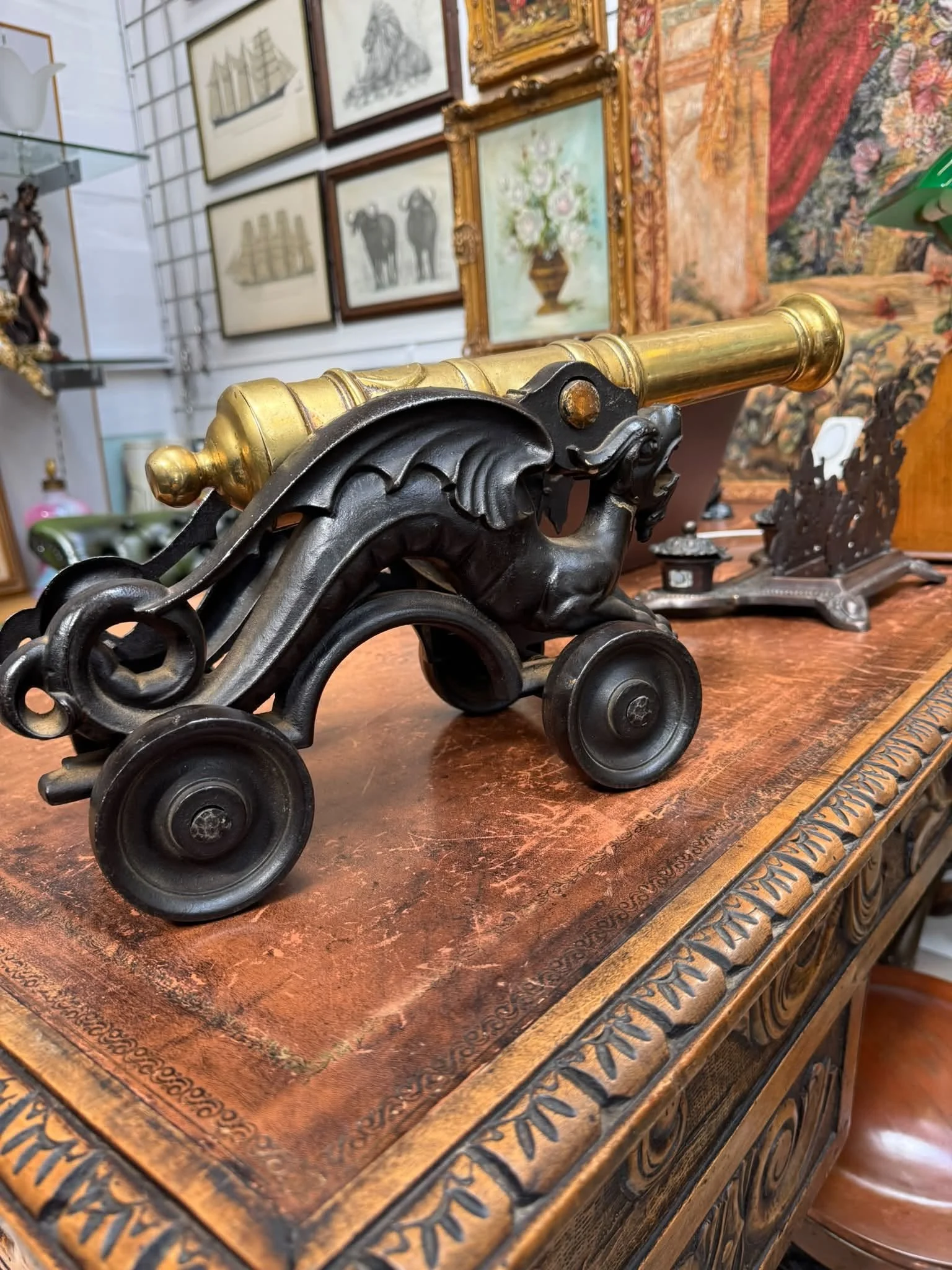 An antique black and gold toy cannon on a carved wooden table in an antique store.