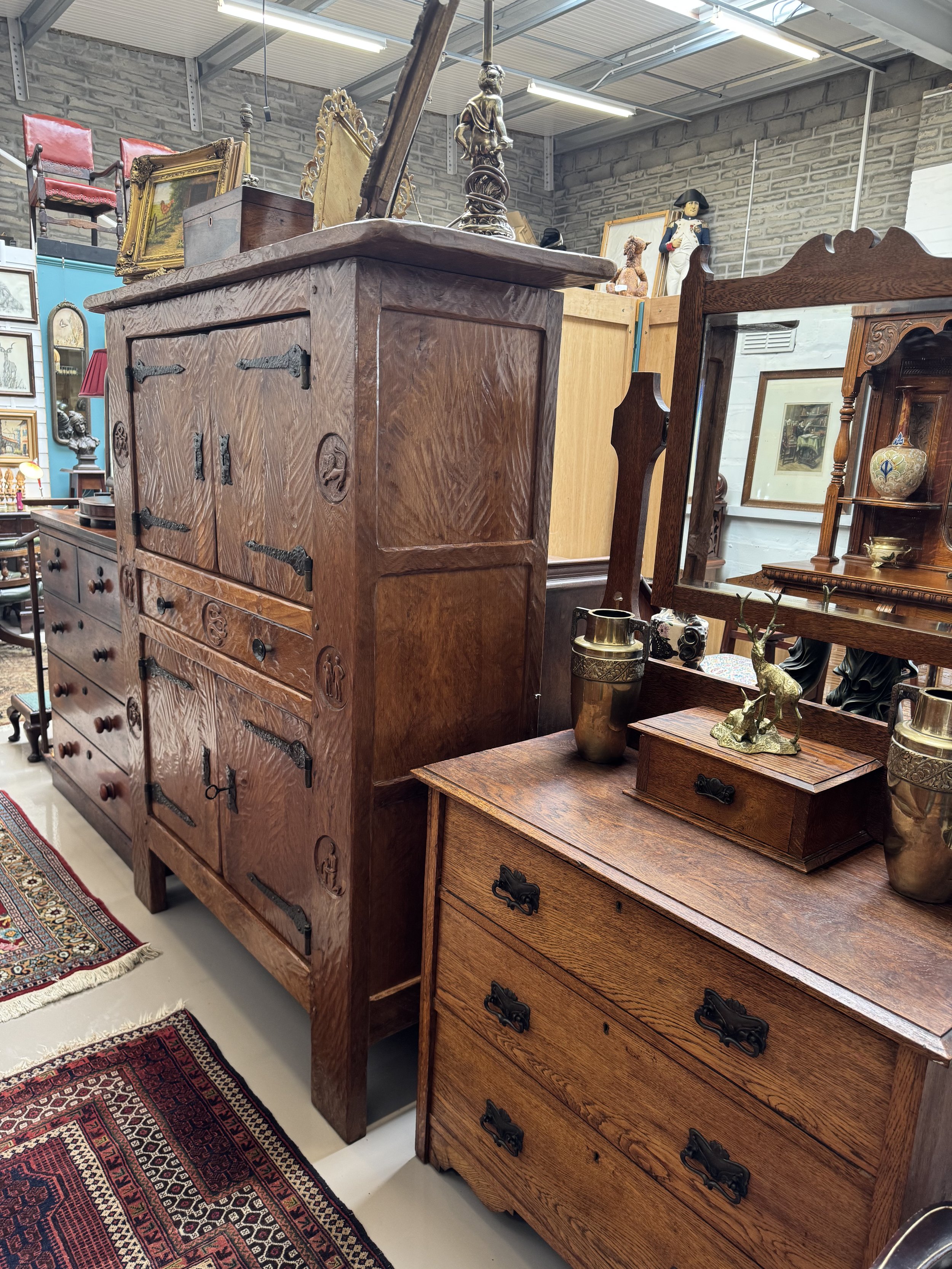 Various antique furniture pieces including a large wooden cabinet, a dresser, framed artwork, a lamp, and decorative items in an antique store.
