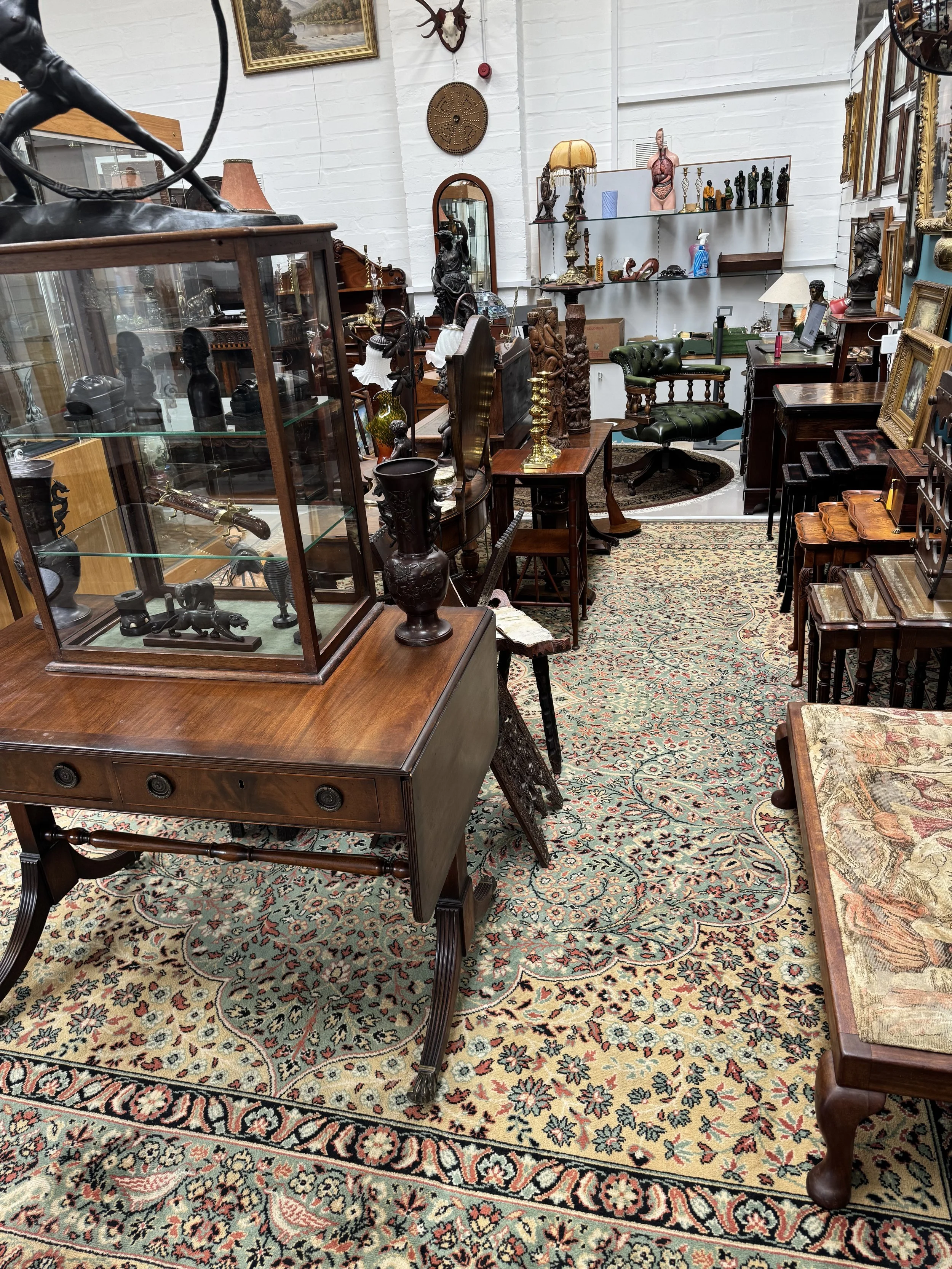 Interior of an antique shop with various wooden furniture, decorative items, and a patterned rug on the floor.