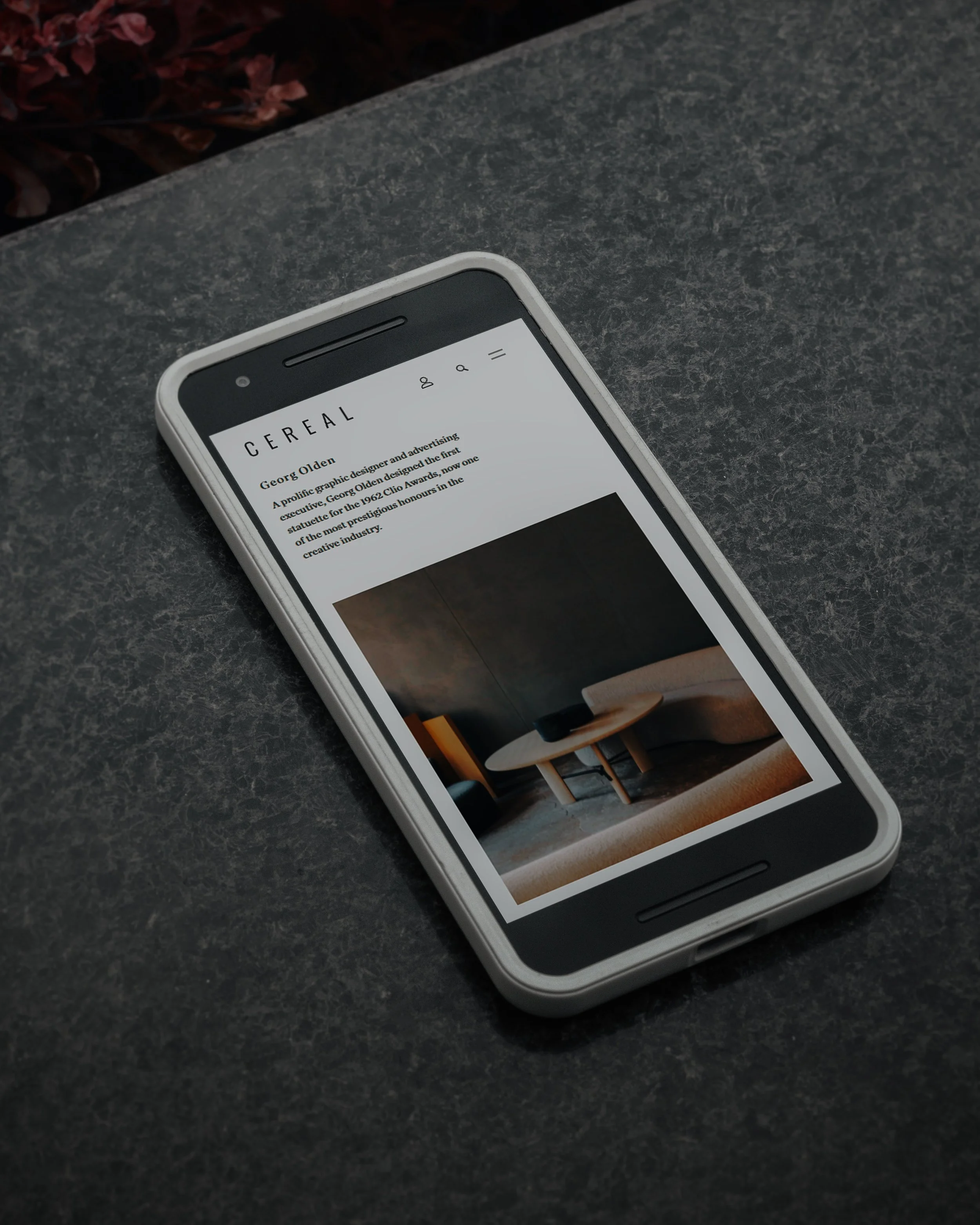 Smartphone placed on a dark, textured surface showing an article about interior design in an app or website.