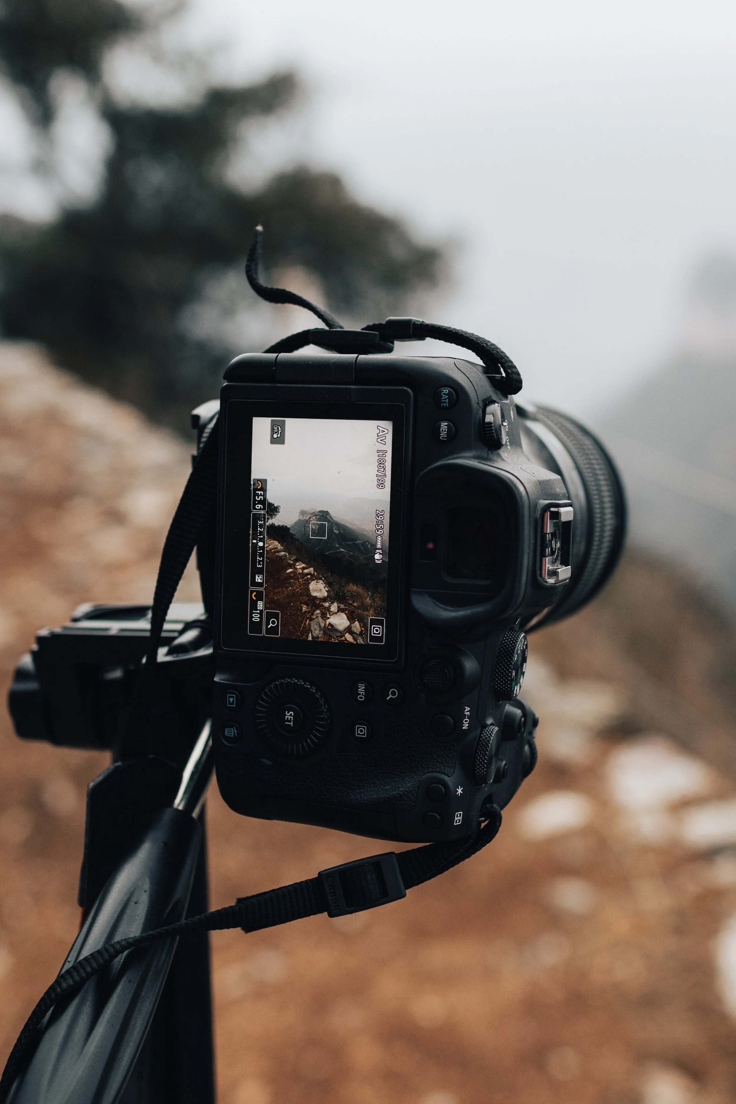 A digital camera mounted on a tripod, focused on an outdoor landscape with a rocky terrain and misty or foggy background.