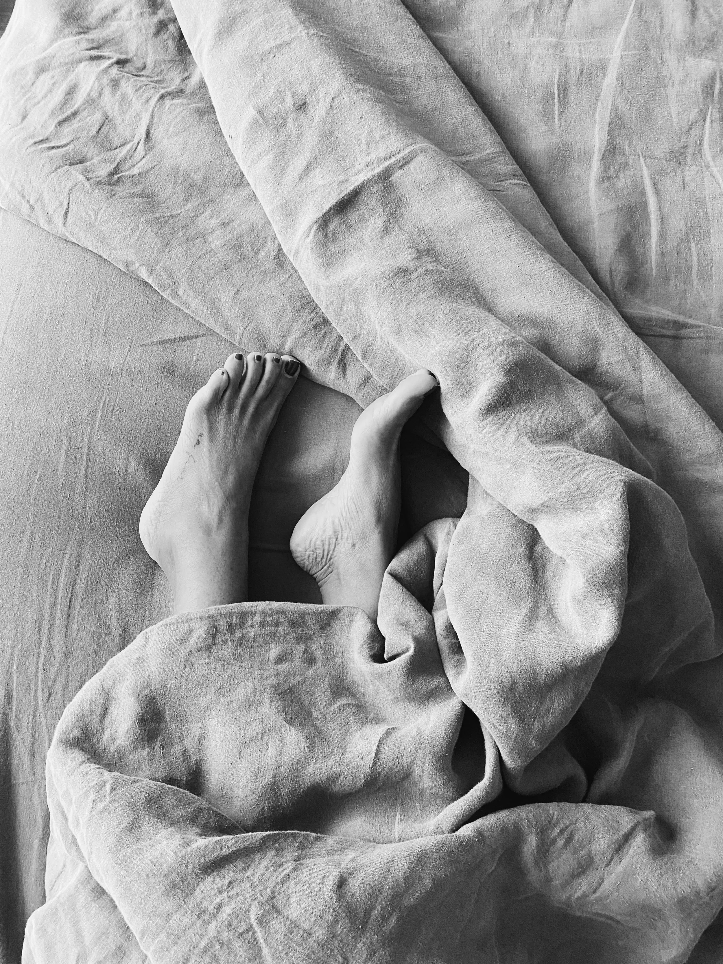 A person with painted toenails standing on a textured surface, partially covered by wrinkled fabric sheets or blankets.