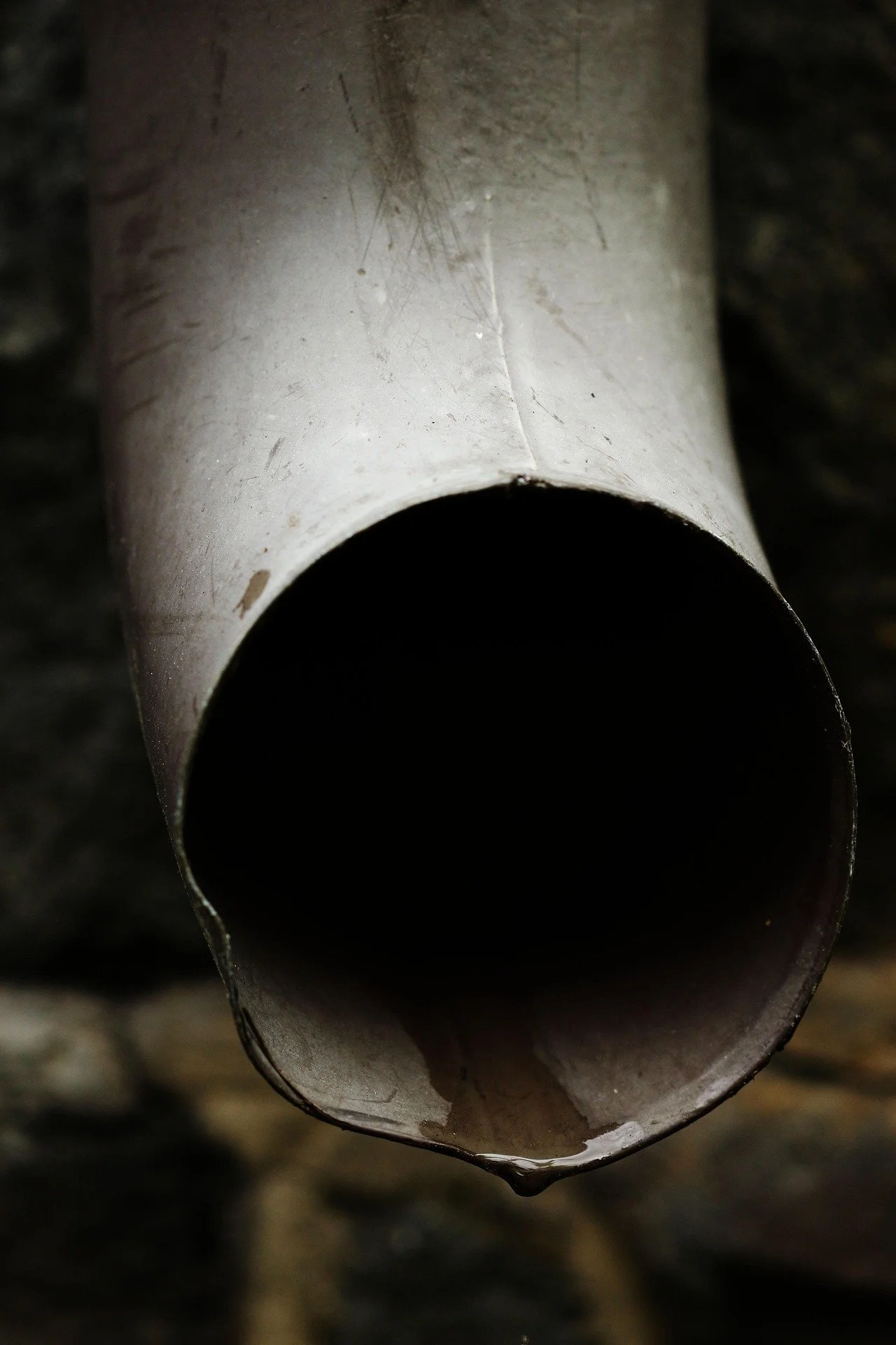 A close-up view of the end of a metallic pipe with some water droplets and dirt on its surface.