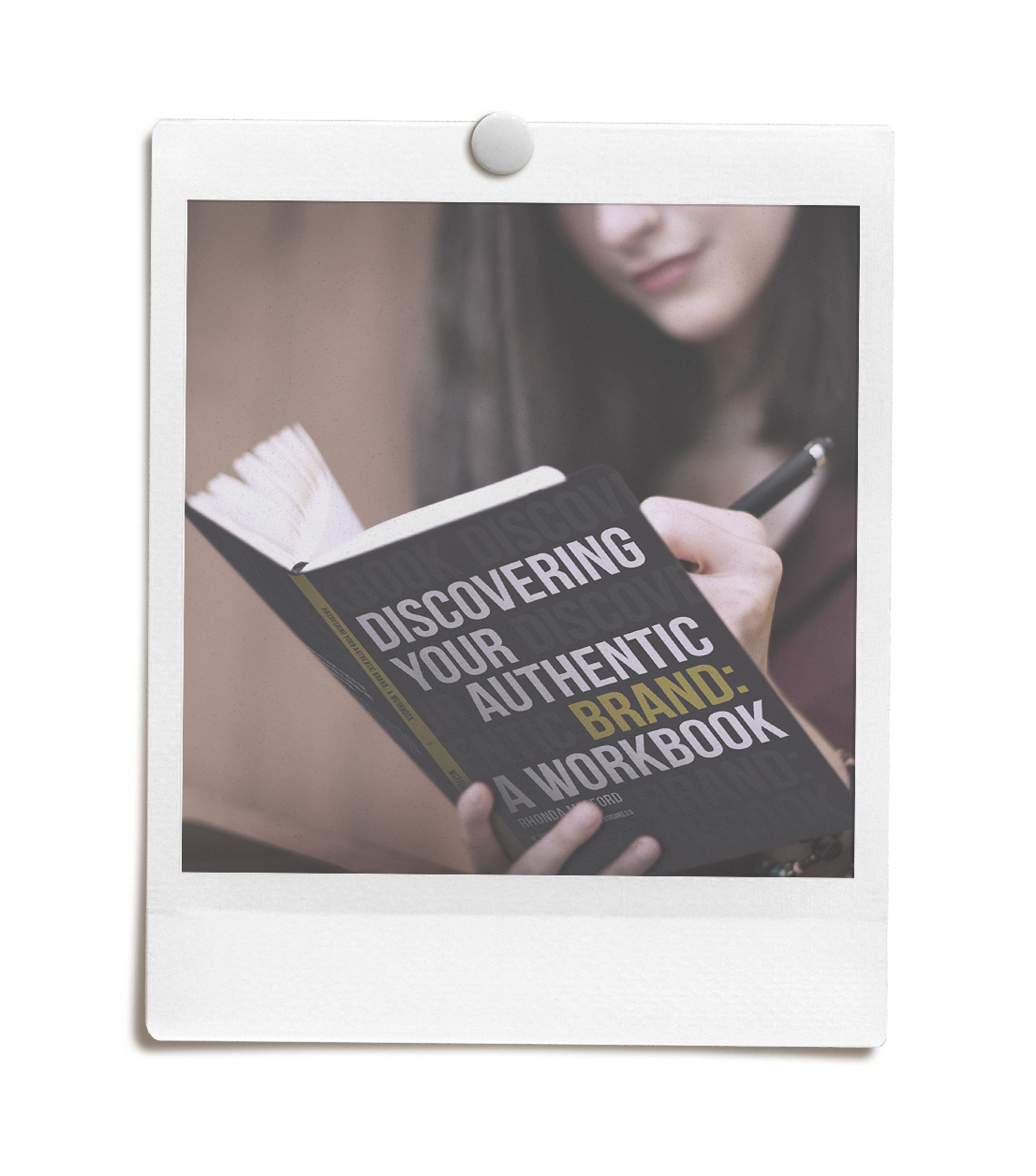 A woman looking at a book titled 'Discovering Your Authentic Brand: A Workbook' with a pen in her hand.