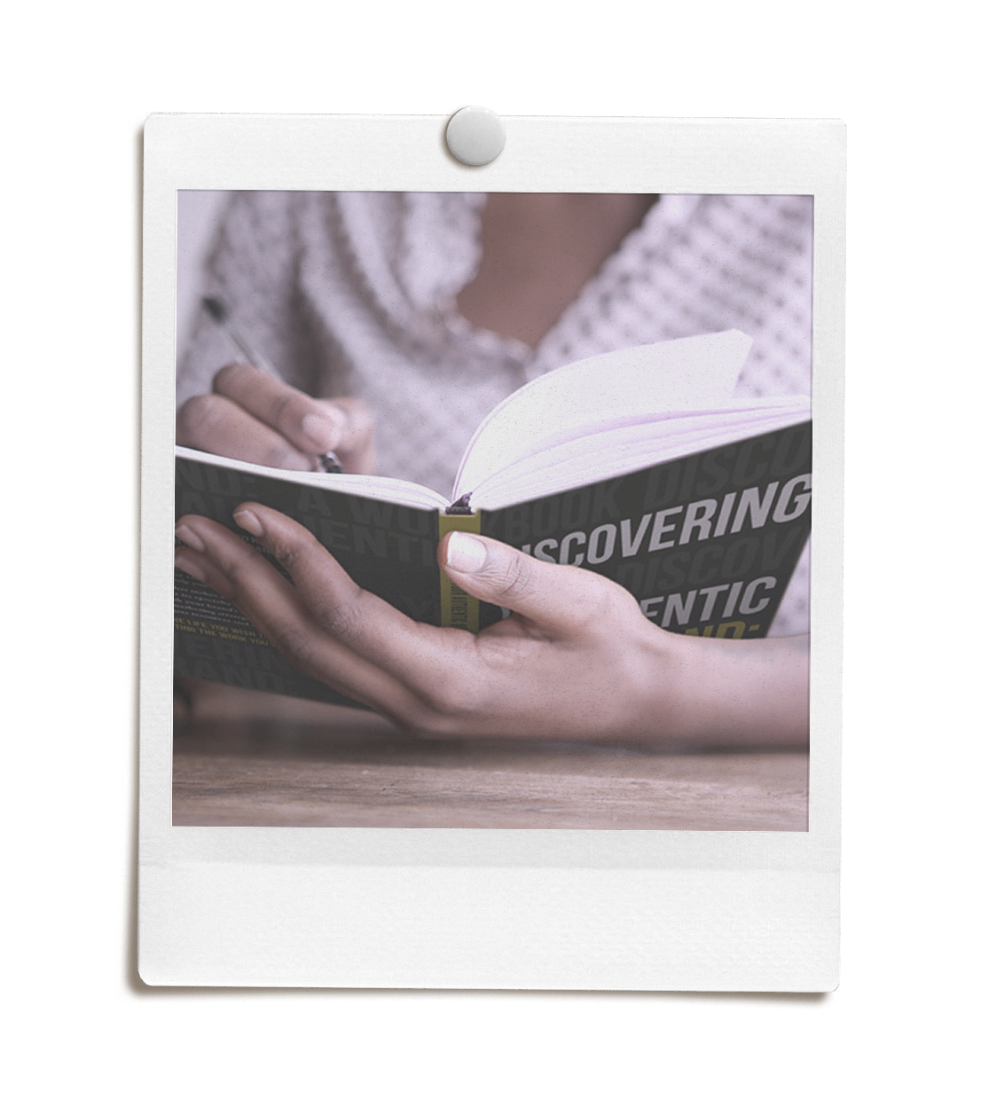Person holding an open book titled "Discovering Your Authentic Brand" while writing in it with a pen.