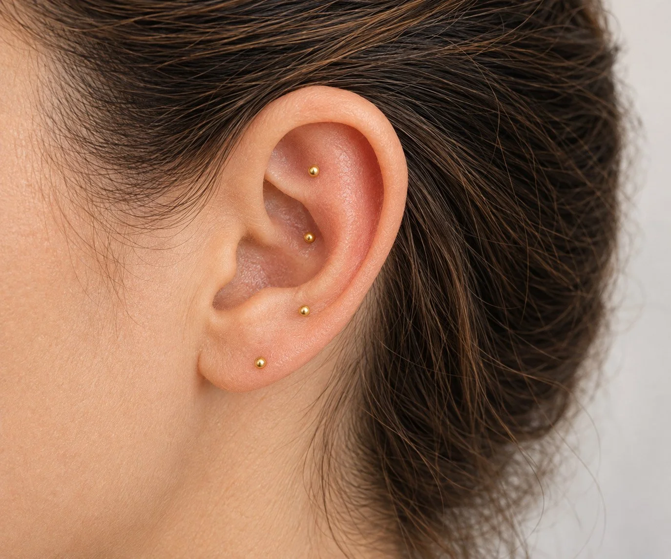 Close-up of a person's ear with four small gold-stud earrings.