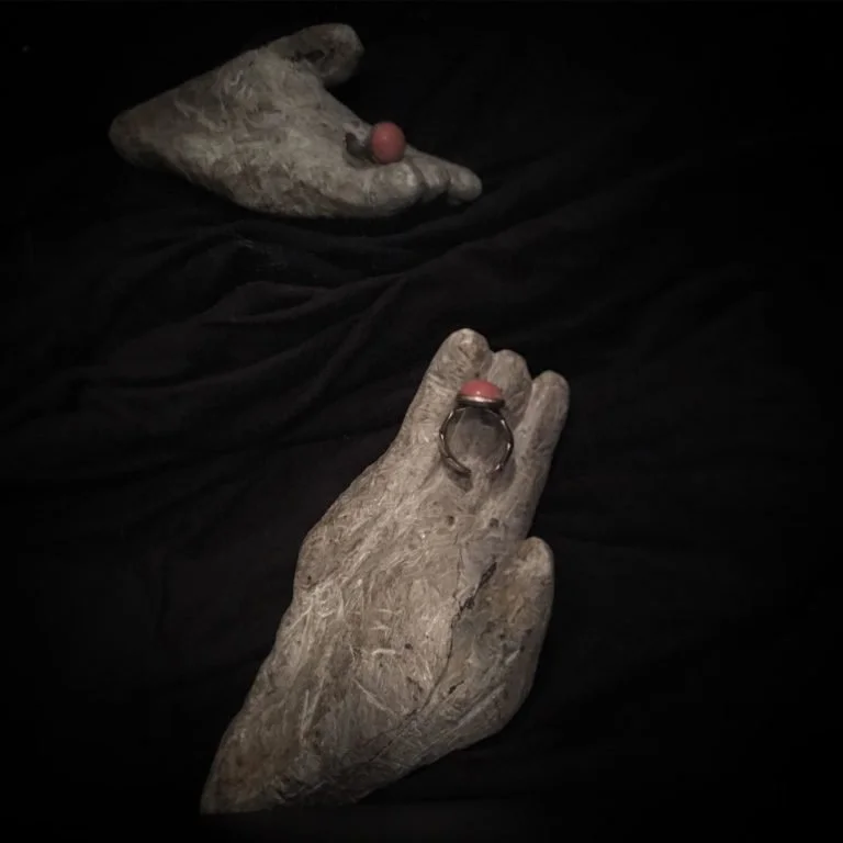 A four-fingered hand carved from rock holds an antique ring before a mirror