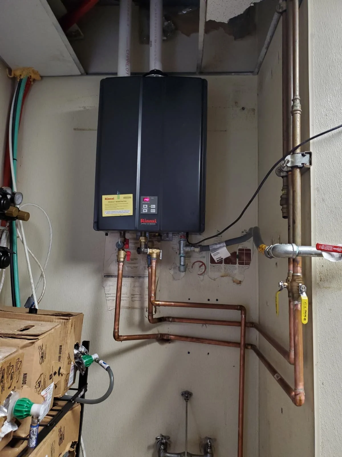 A water heater system mounted on a wall with copper pipes, valves, and a control panel.