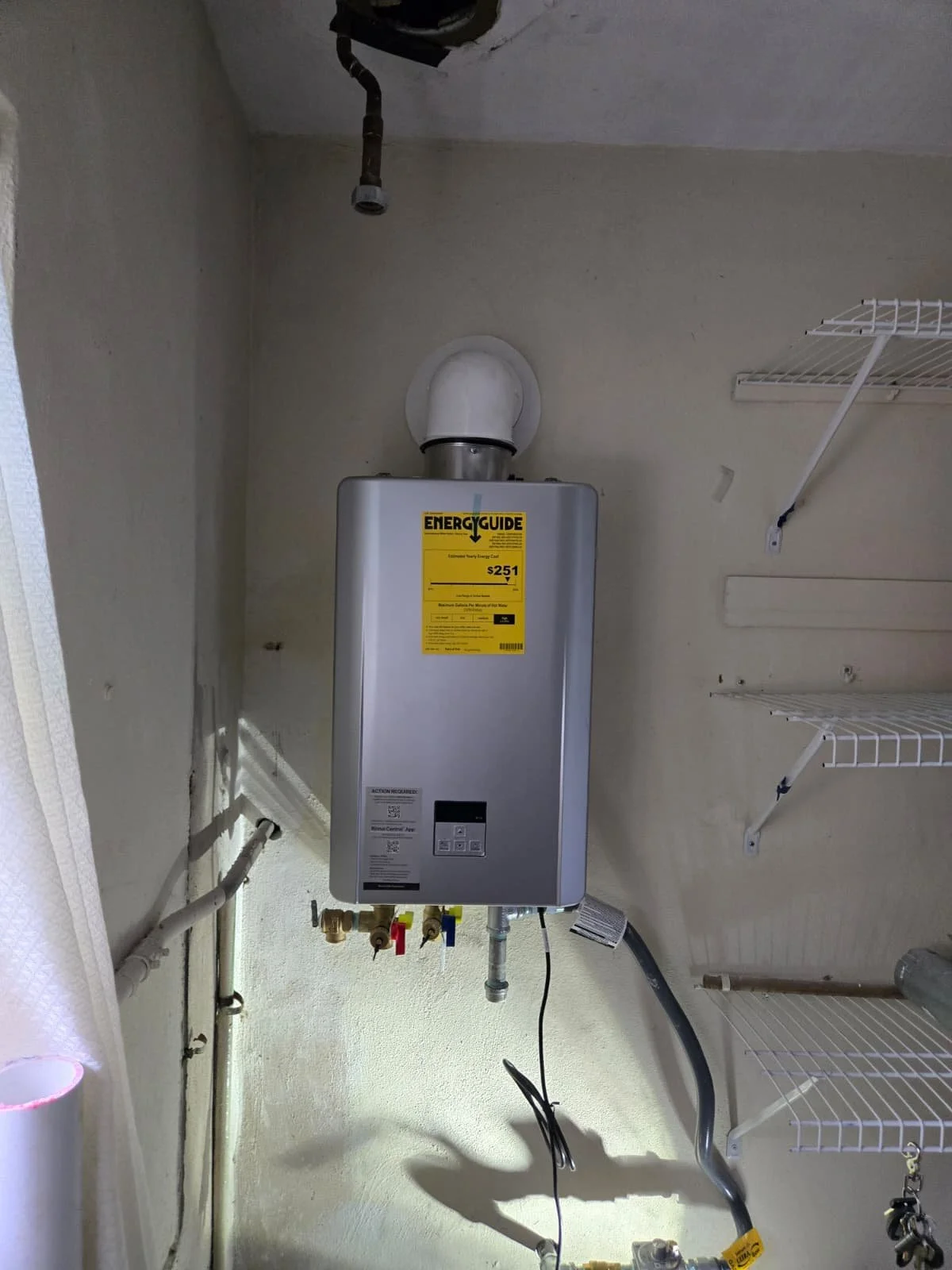 Natural gas boiler with an energy guide sticker, vent pipe, and nearby shelving in a laundry room.