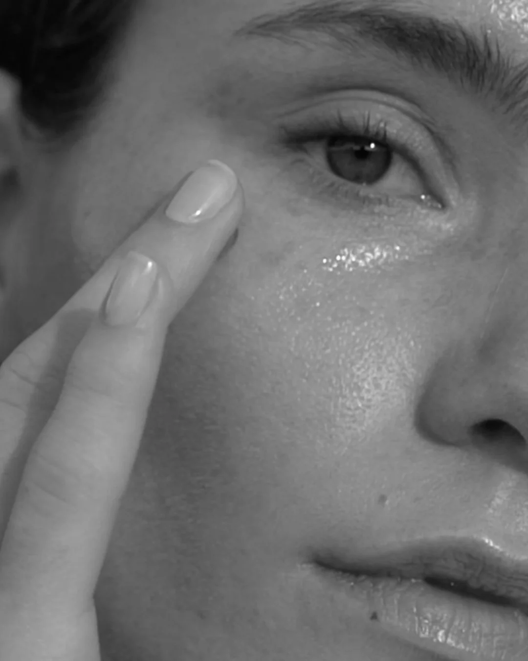 Close-up of a person's face, focusing on their eye and cheek, with a finger touching the skin near the eye.