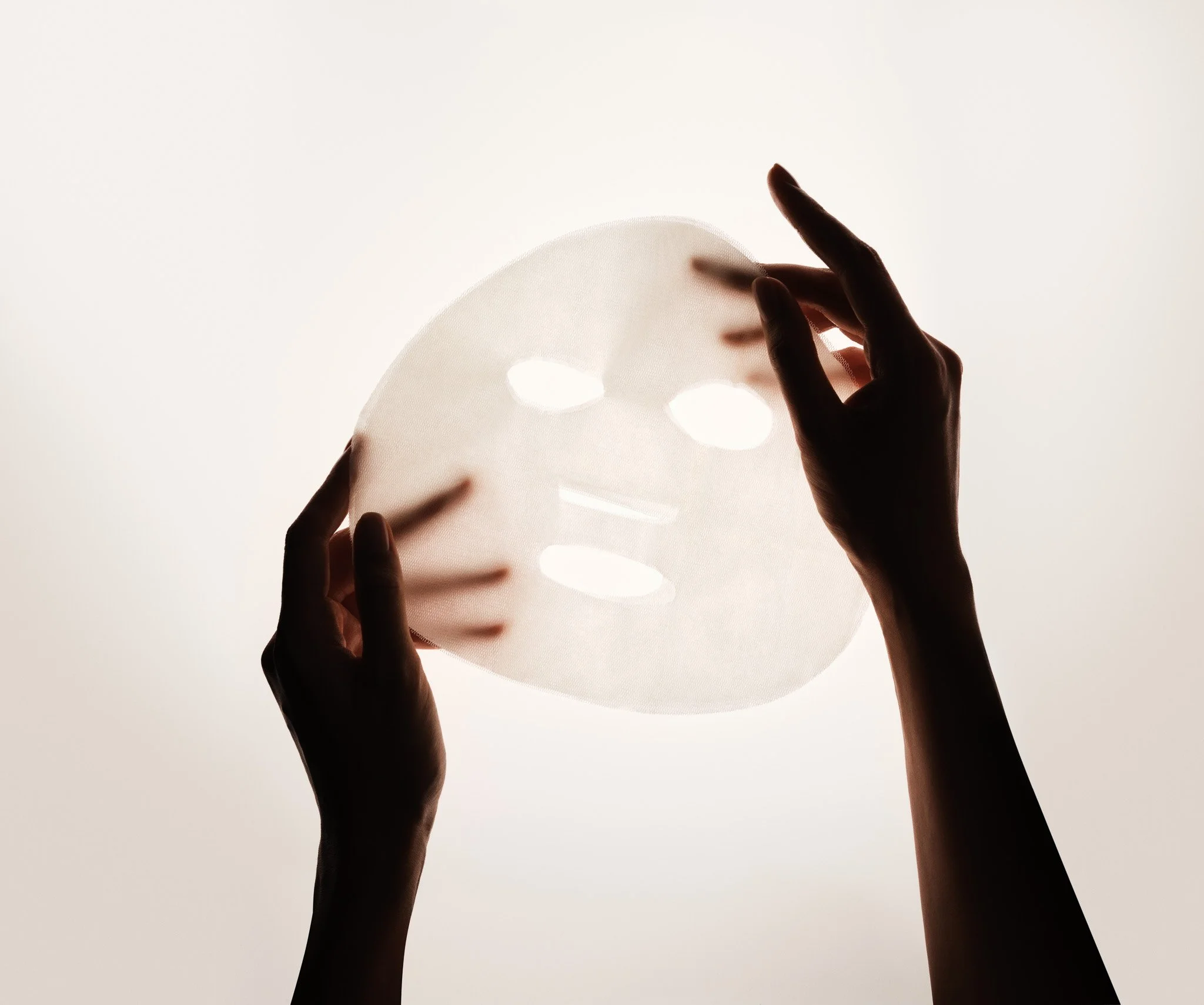 Silhouetted hands holding a semi-transparent, moon-shaped paper lantern against bright light background.