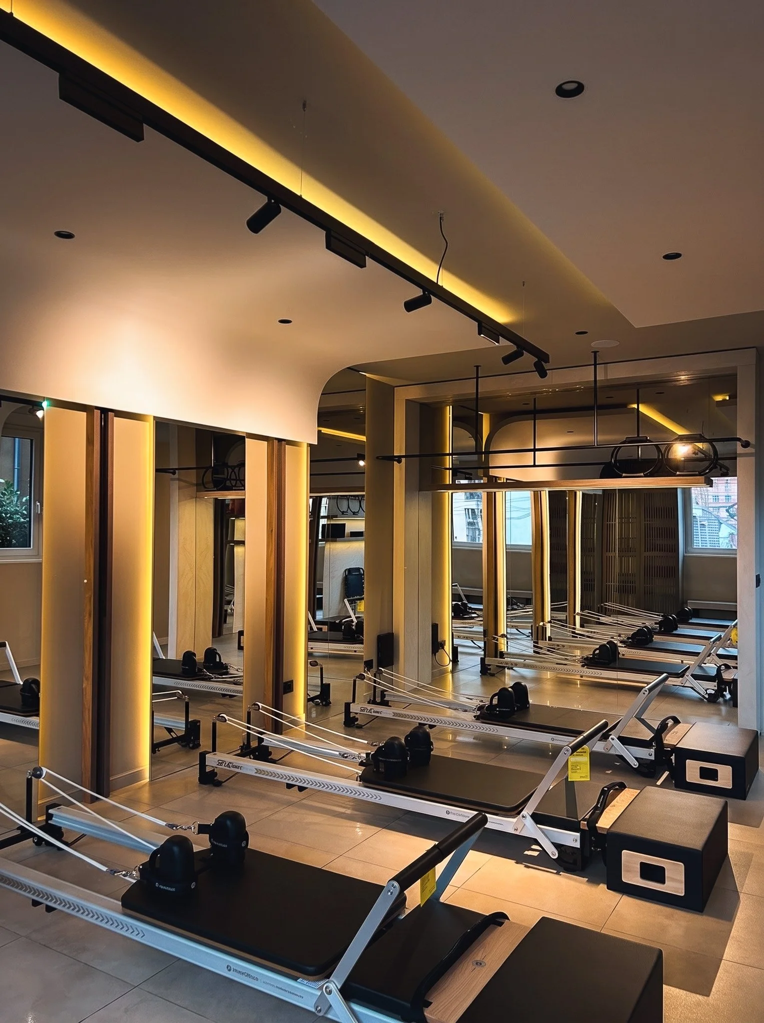 Fitness studio with Pilates reformers, mirrors, ceiling track lighting, and warm ambient lighting.