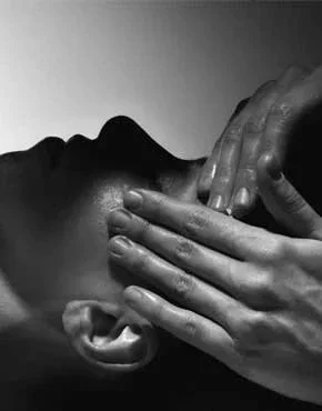 A person receiving a massage on their neck with multiple hands applying pressure.