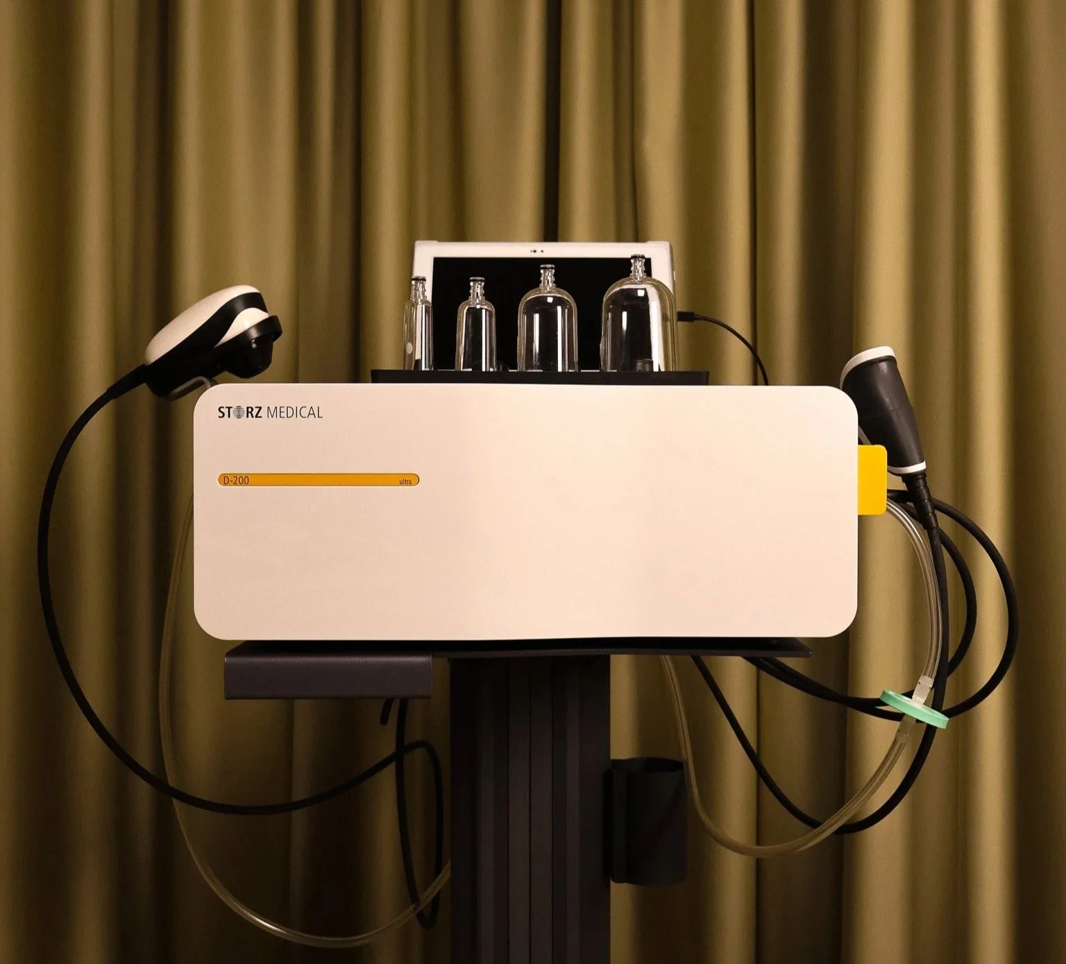 A medical device with four glass vials on top, connected to tubes and sensors, labeled 'STERZ MEDICAL' and 'D-200 ultra,' set against a background of beige curtains.