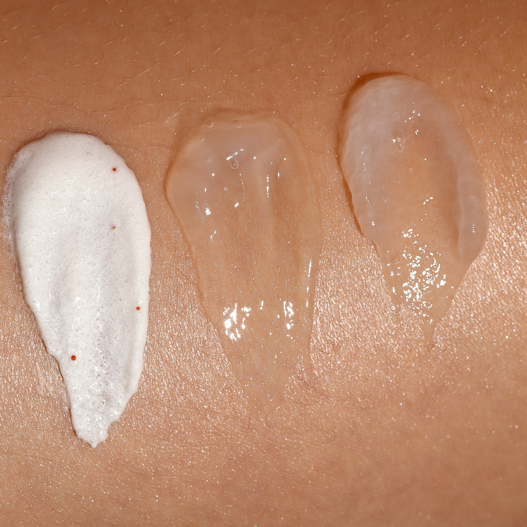 Close-up of three different skincare product textures on skin, including a foamy white cream, a clear gel, and a semi-opaque lotion.
