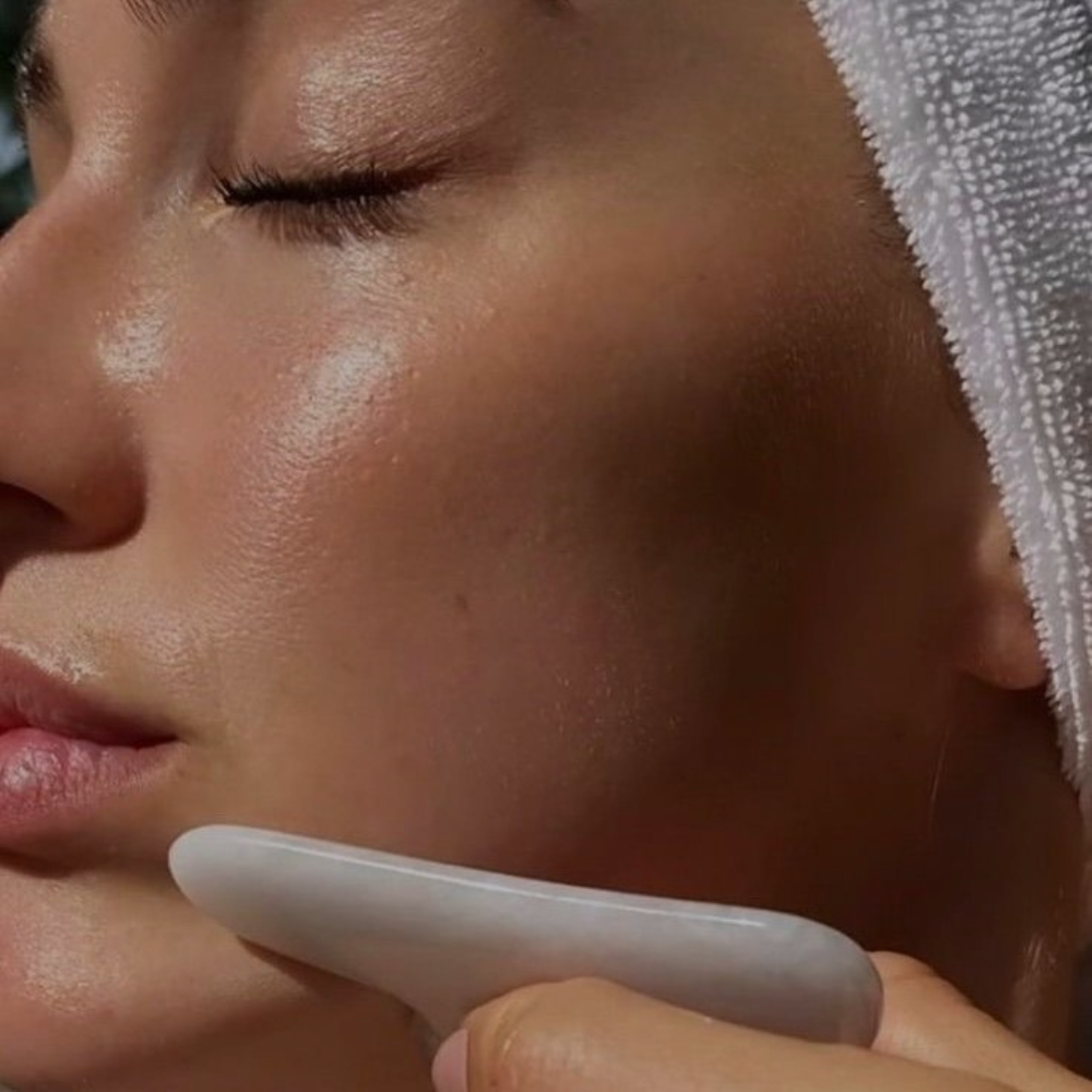 Close-up of a person receiving a facial treatment with a jade roller on their cheek, eyebrows closed, with a towel wrapped around their head.