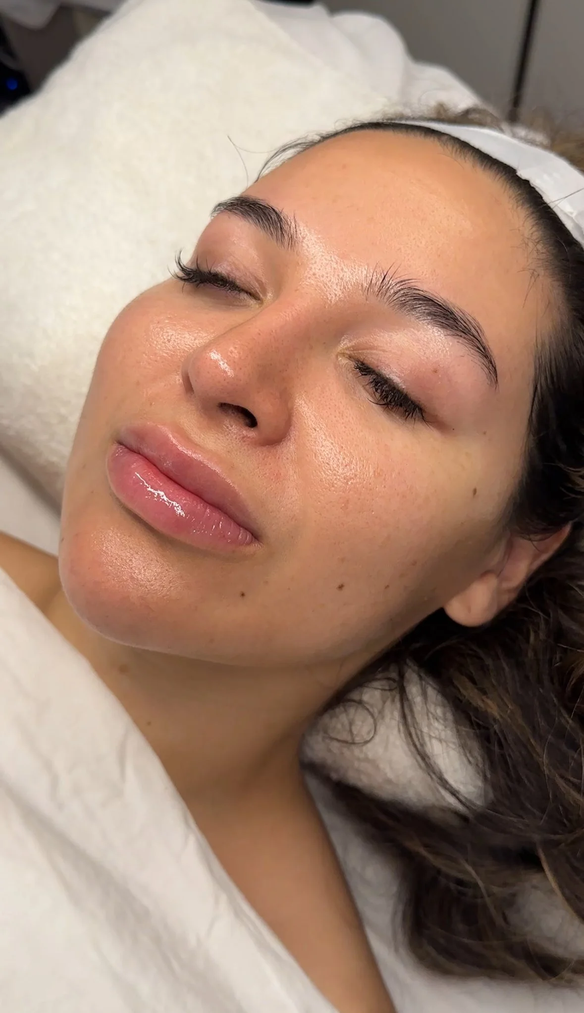 A woman lying down with her eyes closed, appearing relaxed, with her face close-up showing clear, smooth skin and well-groomed eyebrows.