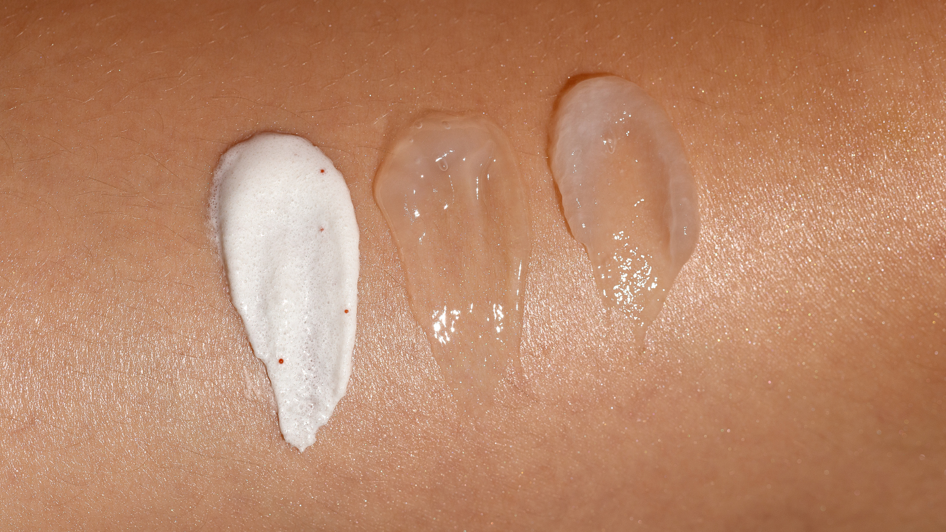 Three types of skincare product drizzled on skin: a white foamy cream, a clear gel, and a thicker translucent gel.