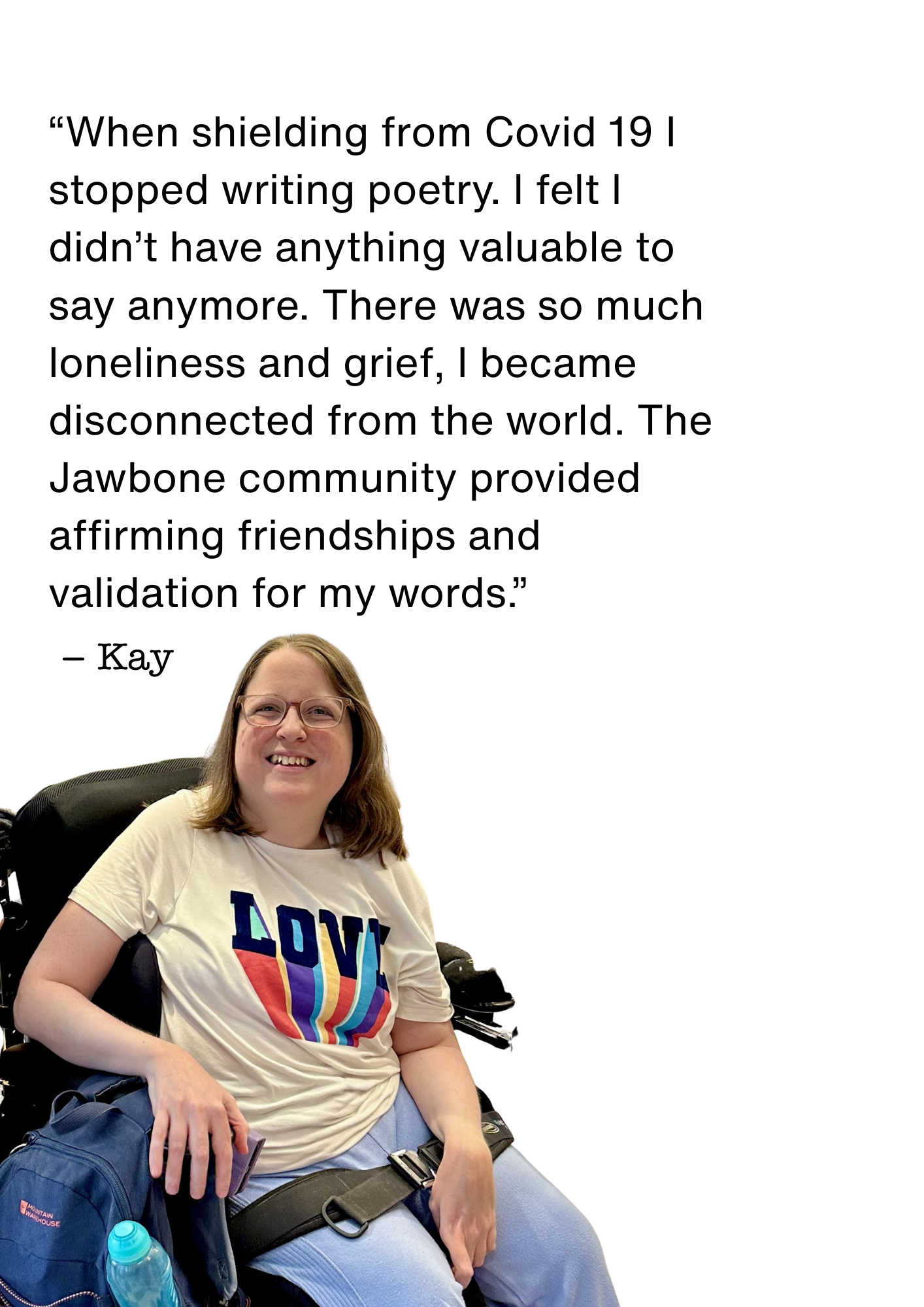 A smiling woman with glasses sitting in a wheelchair, wearing a t-shirt with a rainbow-colored heart and the word 'LOVE'. She has a blue backpack next to her, with a water bottle attached, and is holding a phone.