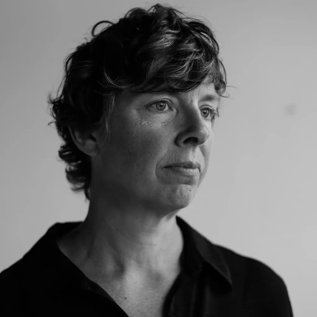 A black and white portrait of a woman with short curly hair, looking to the side with a thoughtful expression. Jessica Taget Rose