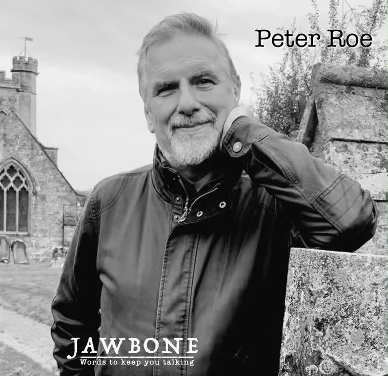 A black and white photo of a middle-aged man with gray hair and a beard, wearing a leather jacket, leaning against a stone wall outdoors with a church and trees in the background. The text on the image says 'Peter Roe' in the top right corner and 'Jawbone' with the subtitle 'Words to keep you talking' at the bottom.