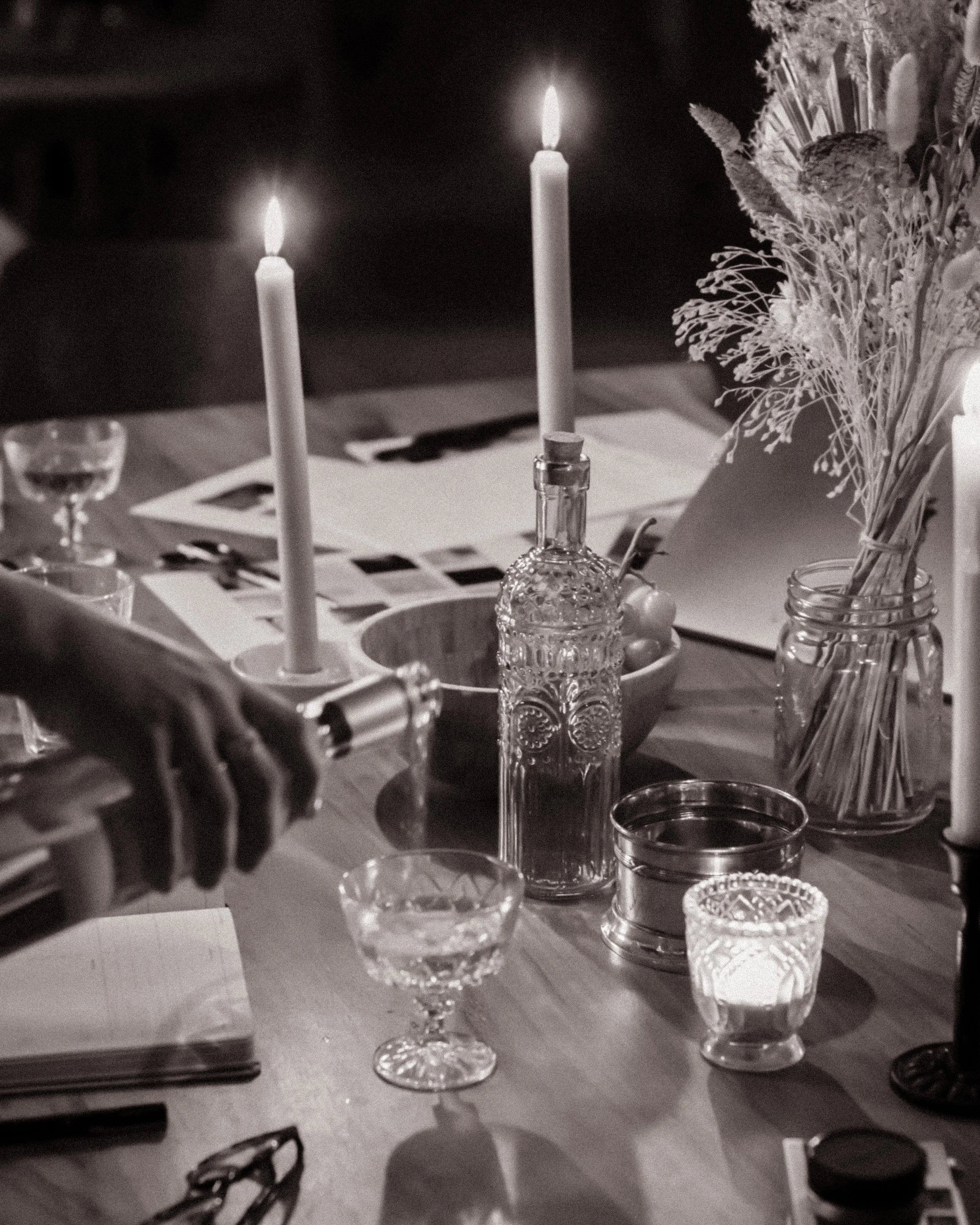 A table decorated with lit candles, glassware, a candlestick, and a flower arrangement.