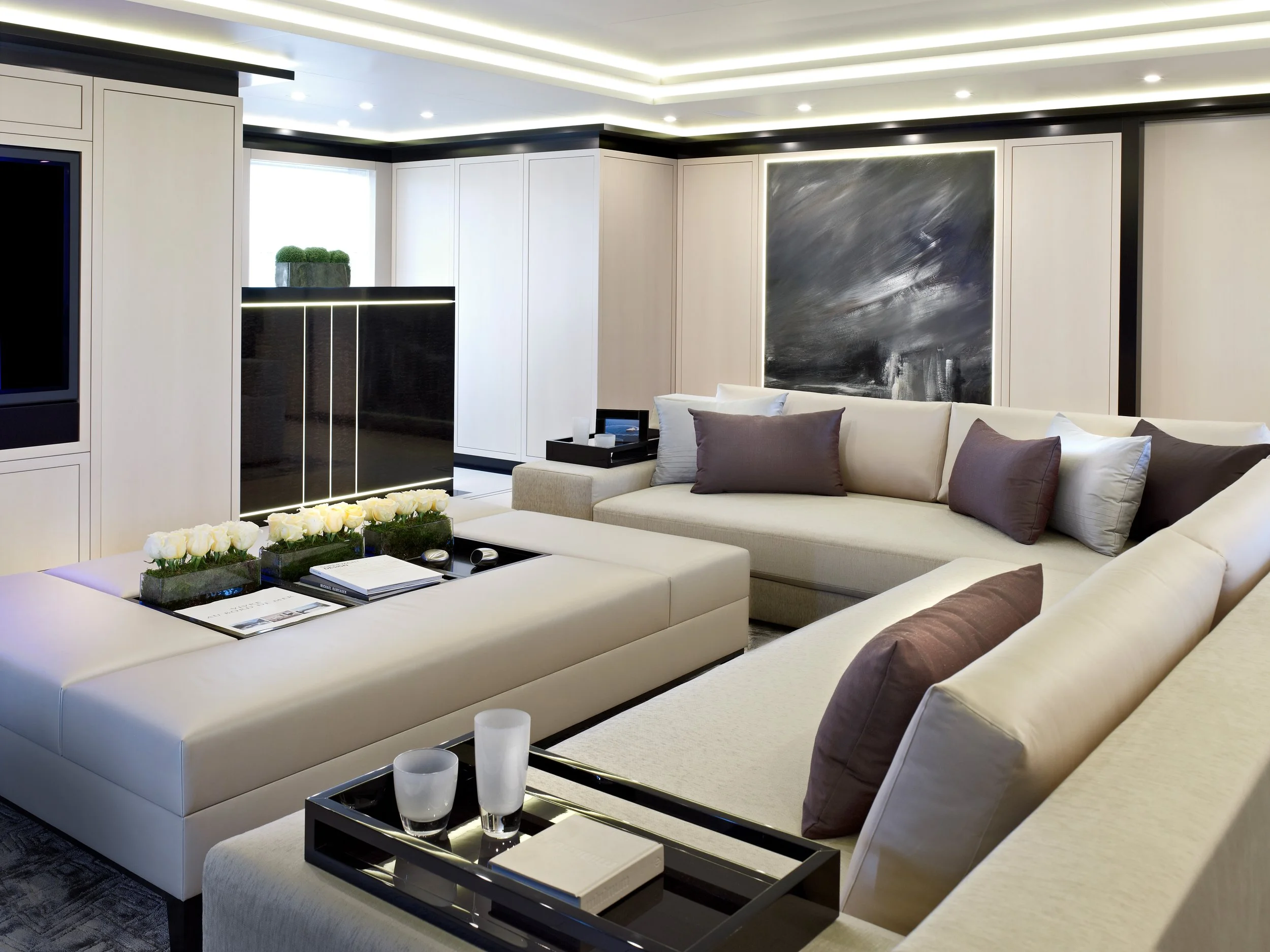 Moderner, eleganter Wohnraum mit weißen Sofas, dunklen Akzenten, schwarzen Beistelltischen, dekorativen Kissen und einer schwarzen Wand mit abstrakter Kunst.