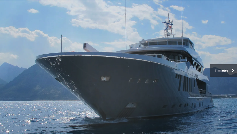 Großer Yacht auf dem Wasser mit Bergen im Hintergrund bei sonnigem Himmel.