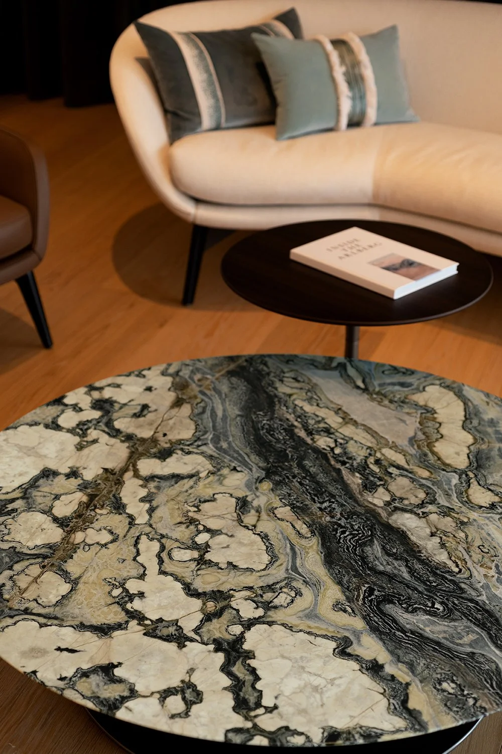 Ein runder Tisch mit einer aufliegenden Zeitschrift in einem Wohnzimmer mit einem beige Sofa und Kissen im Hintergrund.