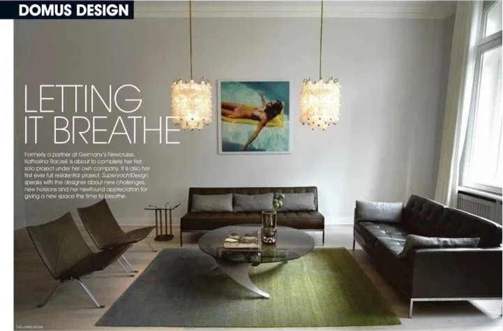 Ein modernes Wohnzimmer mit grauen und schwarzen Sofas, einem runden Couchtisch, grüner Teppich, zwei hängenden Lampen, einem Wandbild und einem großen Fenster.