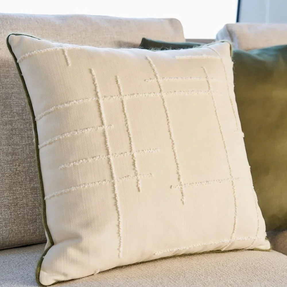 Ein cremefarbener Kissen mit einer geometrischen Stickerei auf einem Sofa