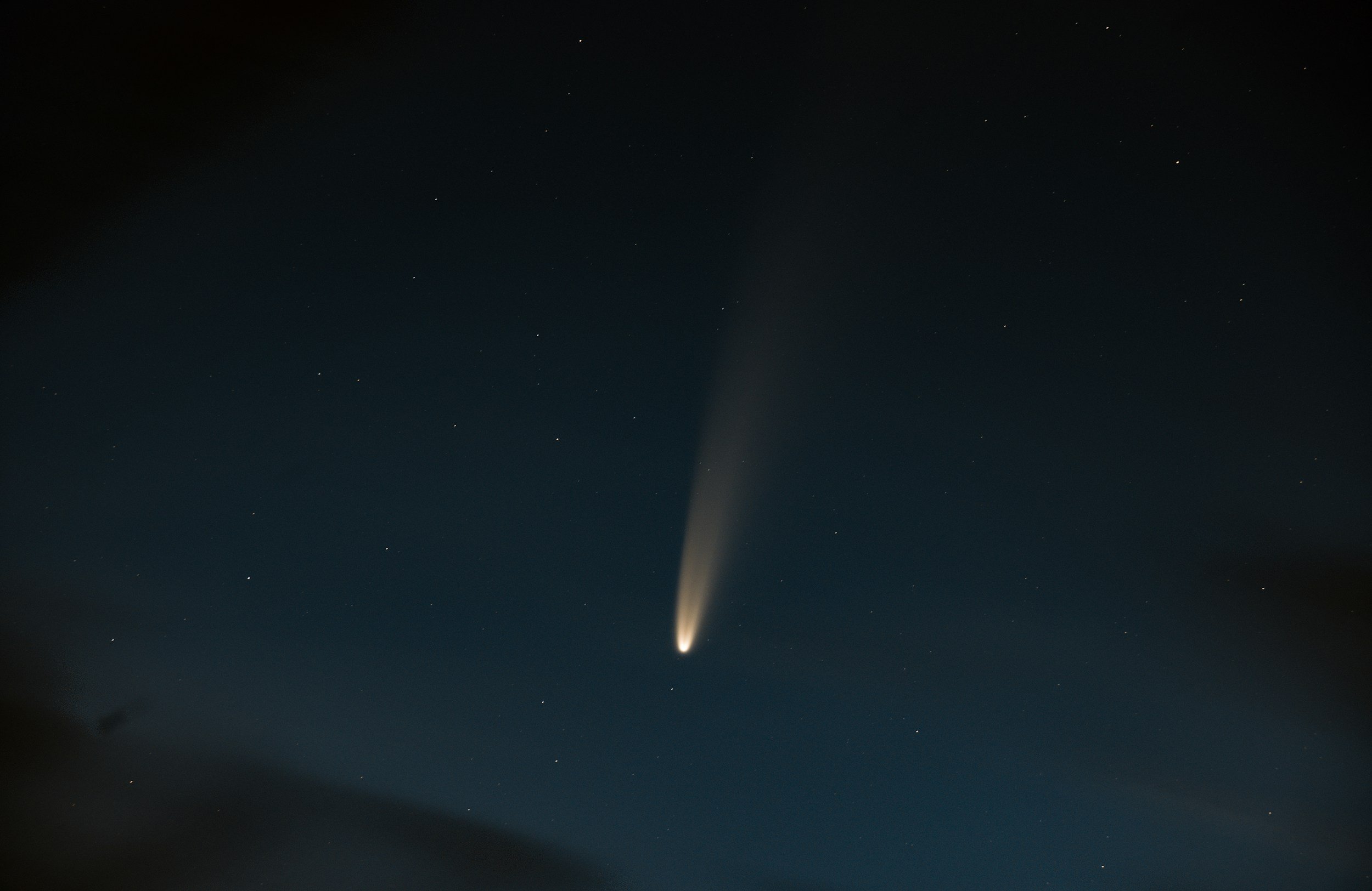 A bright comet with a long tail visible in a clear night sky filled with stars.