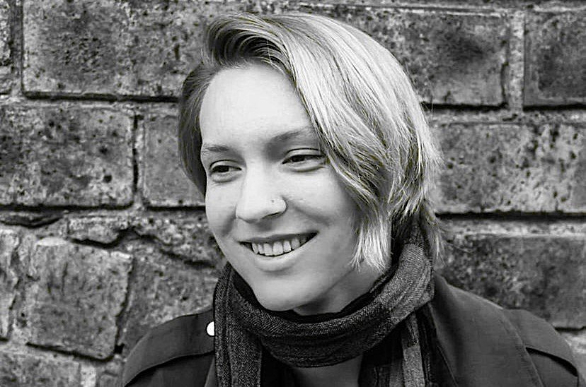 A woman with short blond hair smiling, standing in front of a brick wall.