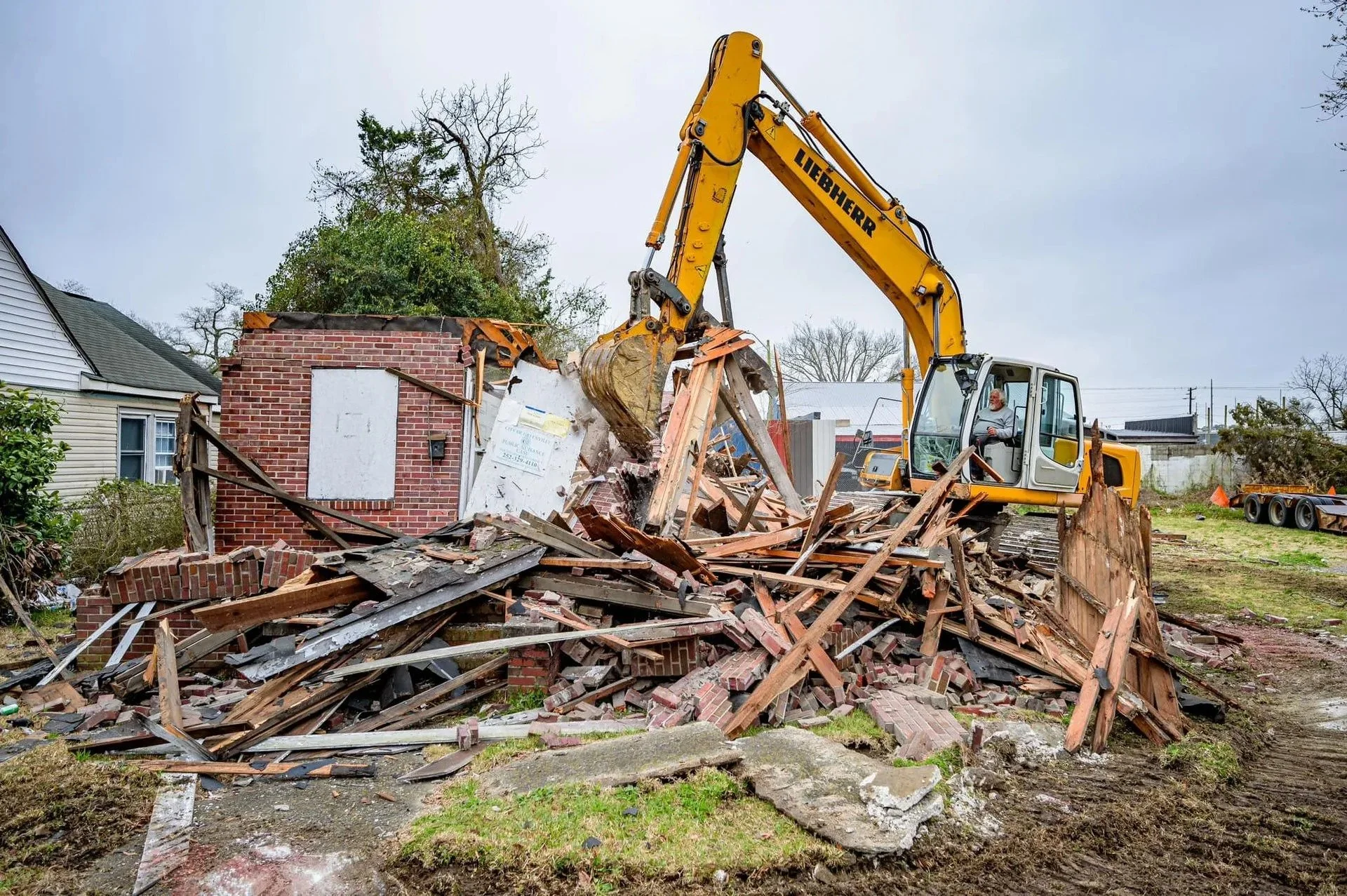 A yellow excavator demolishing a brick building with debris scattered around.