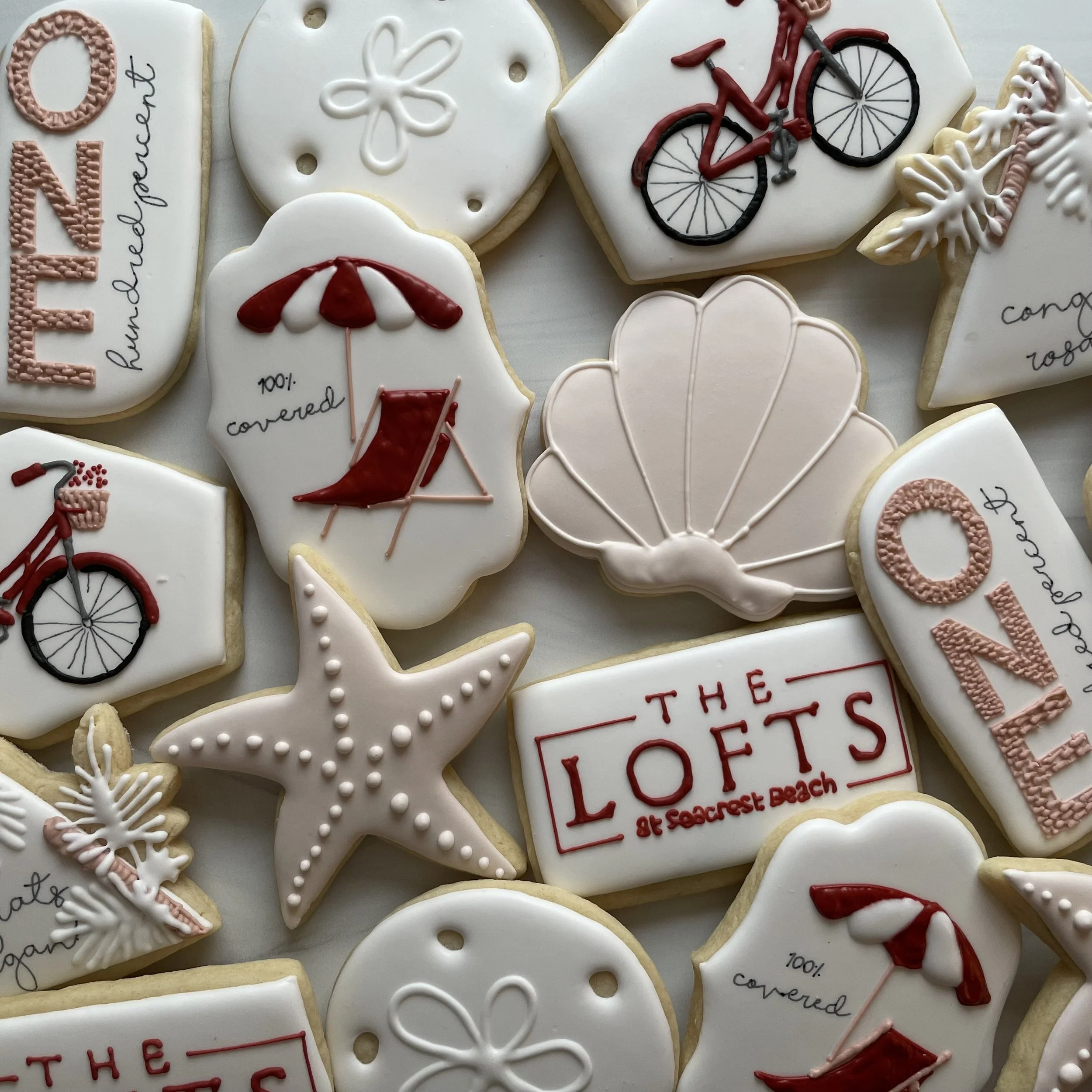 Decorated cookies featuring bicycles, umbrellas, snowflakes, and handwritten messages, arranged closely together on a surface.