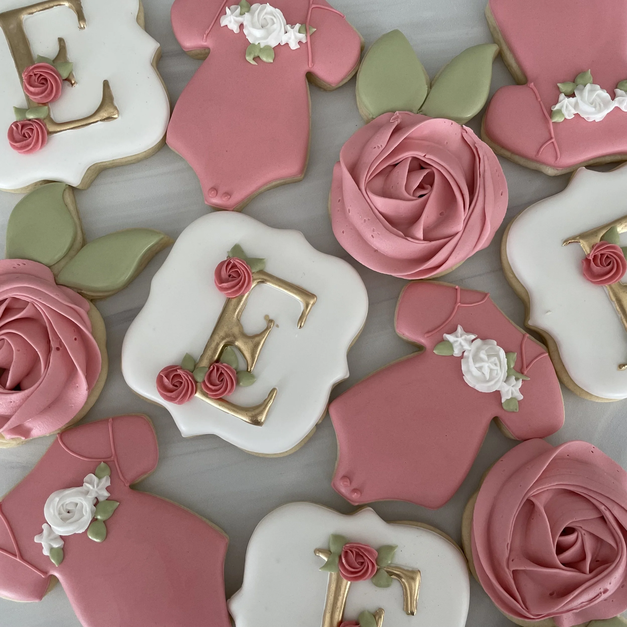 Decorated cookies with pink, white, and green icing, shaped like roses, leaves, and a number '4'. Some cookies have gold accents and floral designs.