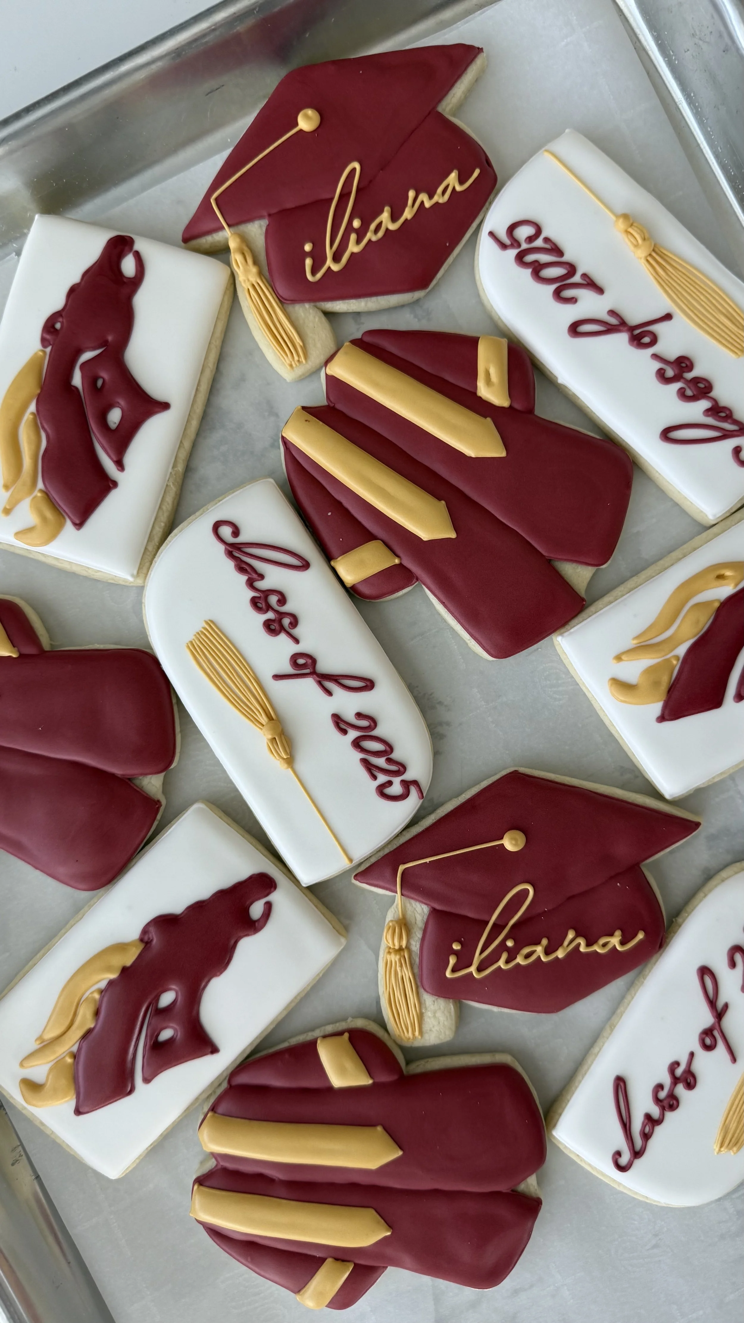 Decorated cookies with graduation cap, diploma, and gown themes, personalized with the name 'Iliana' and the graduation year '2023' on some cookies.