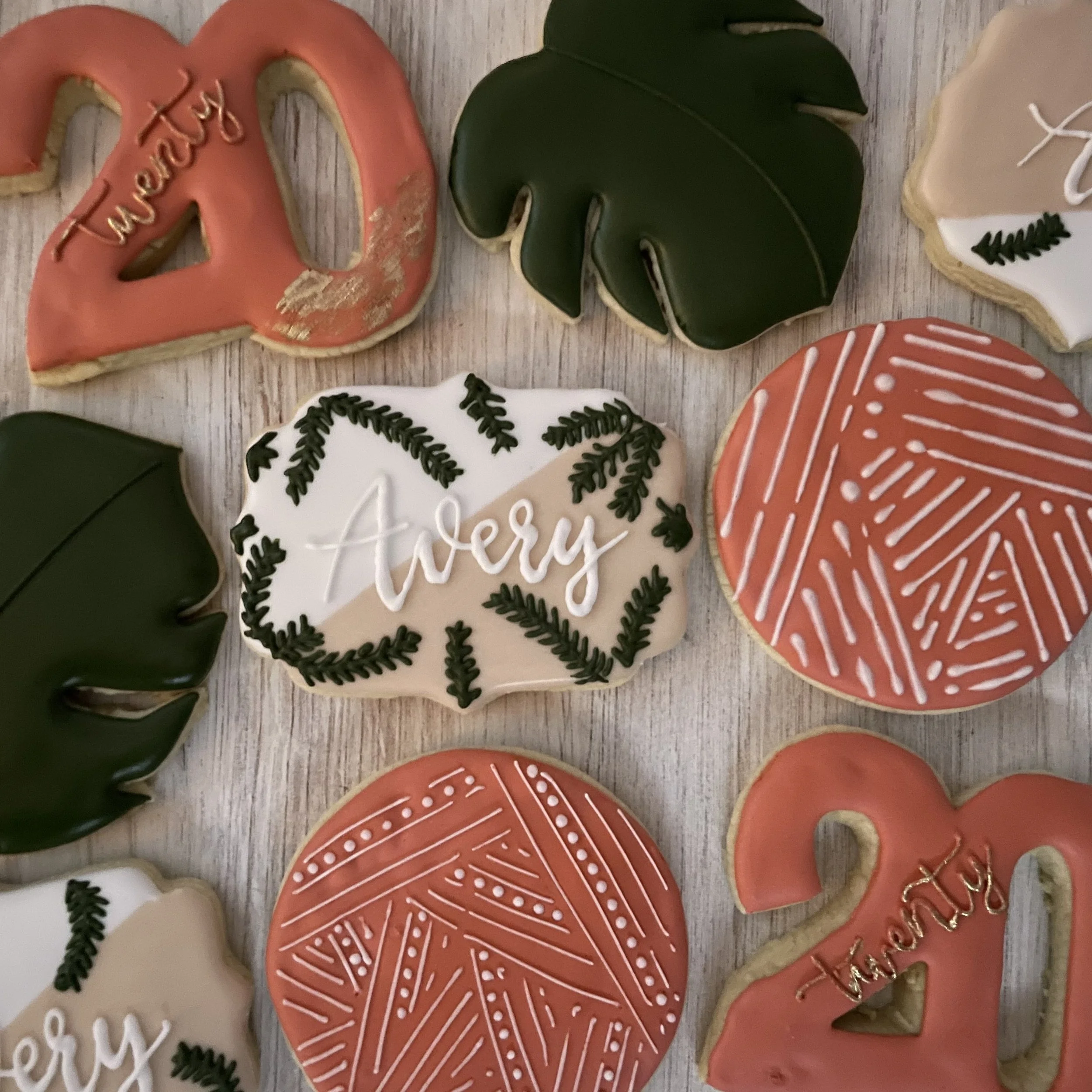 Decorative holiday cookies with Christmas themes including a red ornament with the word 'merry' written on it, a green ornament, and some cookies with pine branch designs and the words 'season' and other holiday-related decorations.